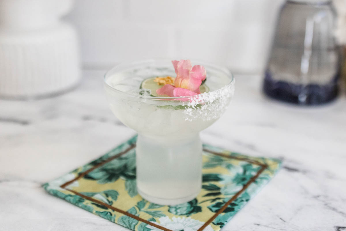 A stemless margarita glass with a partial salt rim on a napkin with pretty garnish.