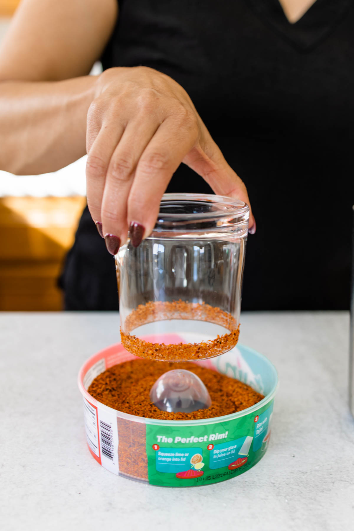 Woman dipping a cocktail glass in a container of Tajin for a margarita.