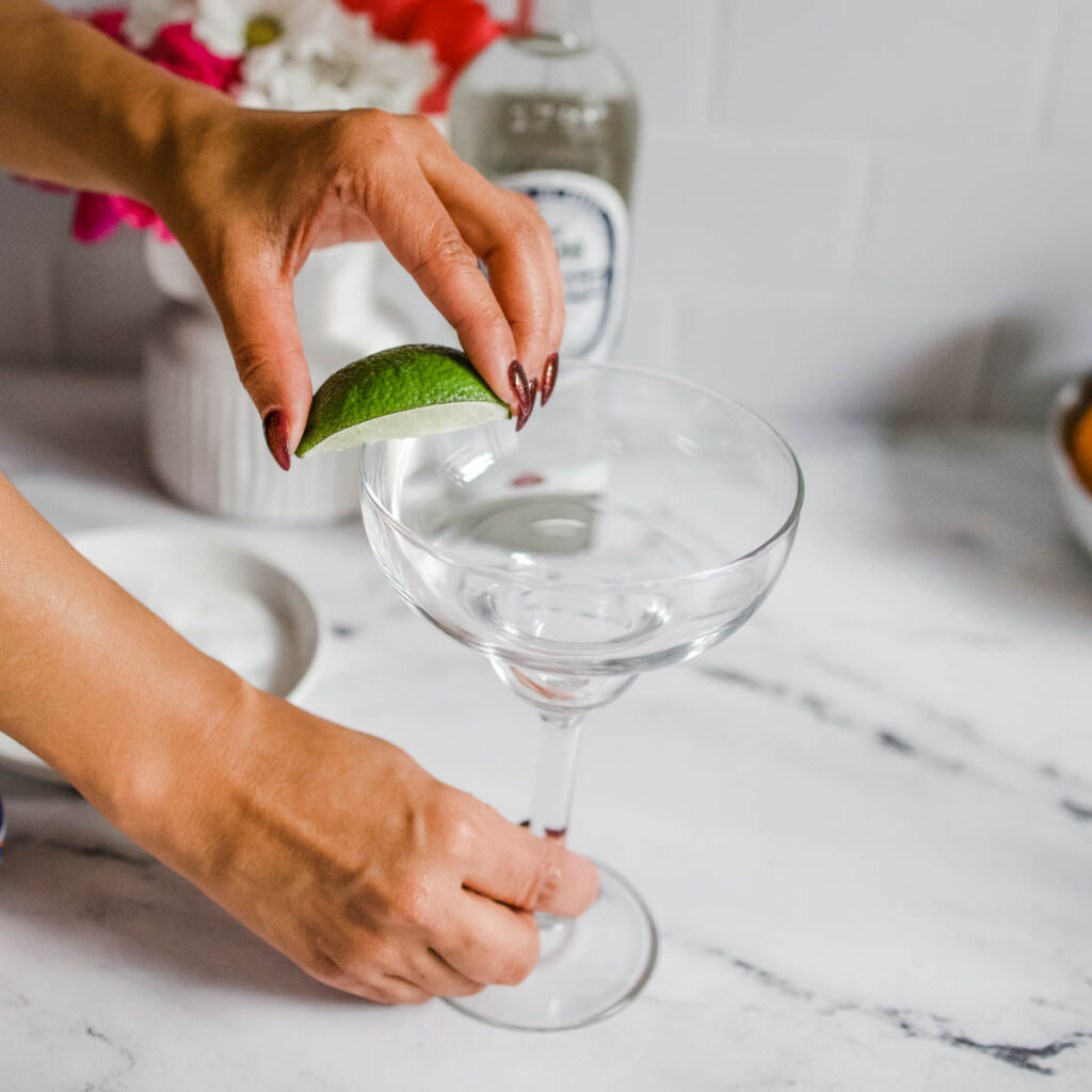 A woman rubbing lime on a margarita glass rim to add salt to it.