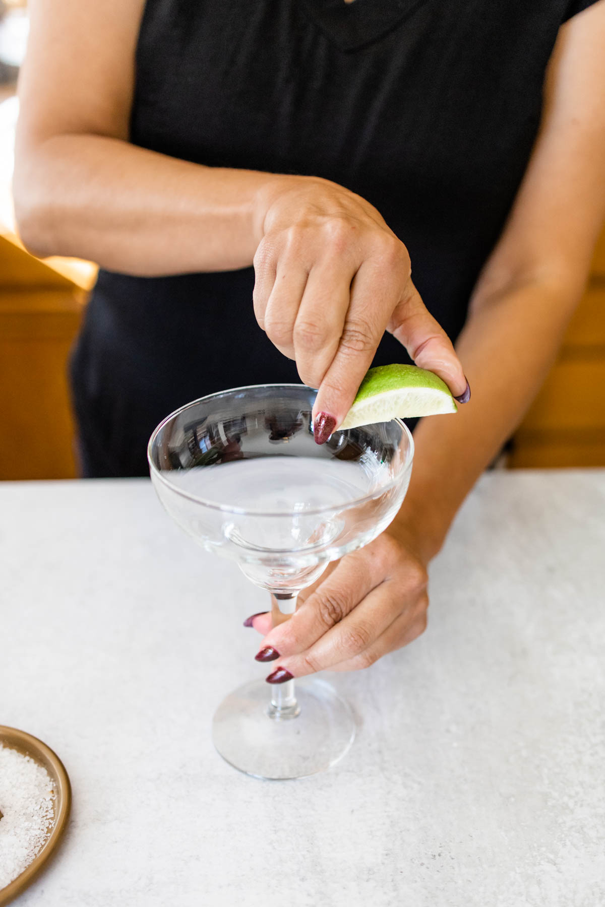 Rubbing a lime wedge on the rim of a margarita glass to add a salt rim.