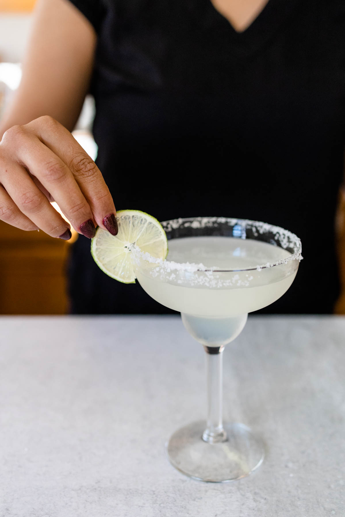 Woman adding a lime wheel to the side of a salt rimmed margarita glass.