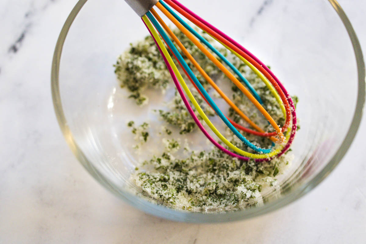 A bowl of basil sugar with a colorful whisk.