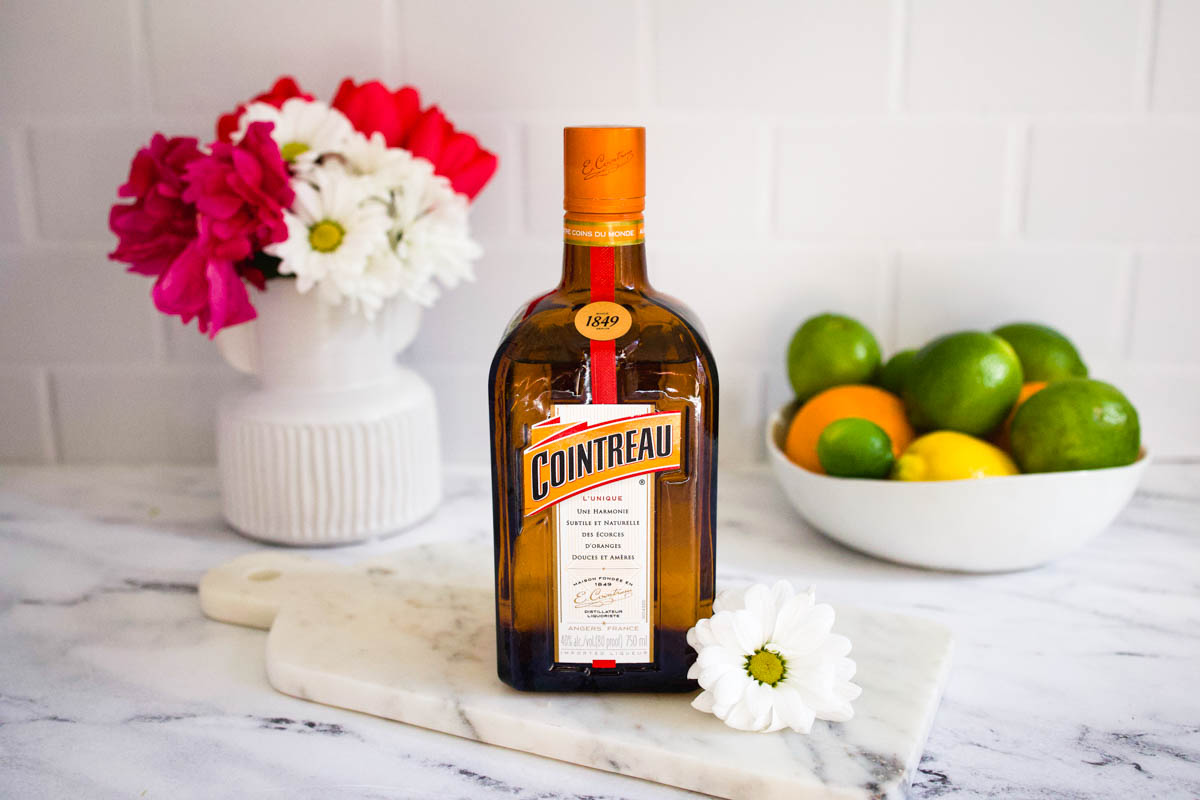 Bottle of Cointreau on a table next to a bowl of citrus fruit.