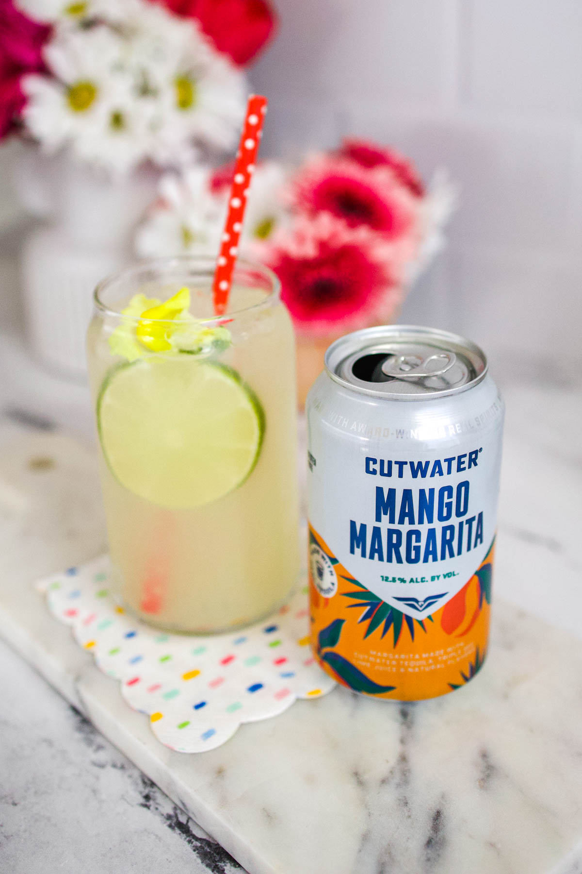 A can of Cutwater Mango Margarita on a table next to a glass holding the cocktail.