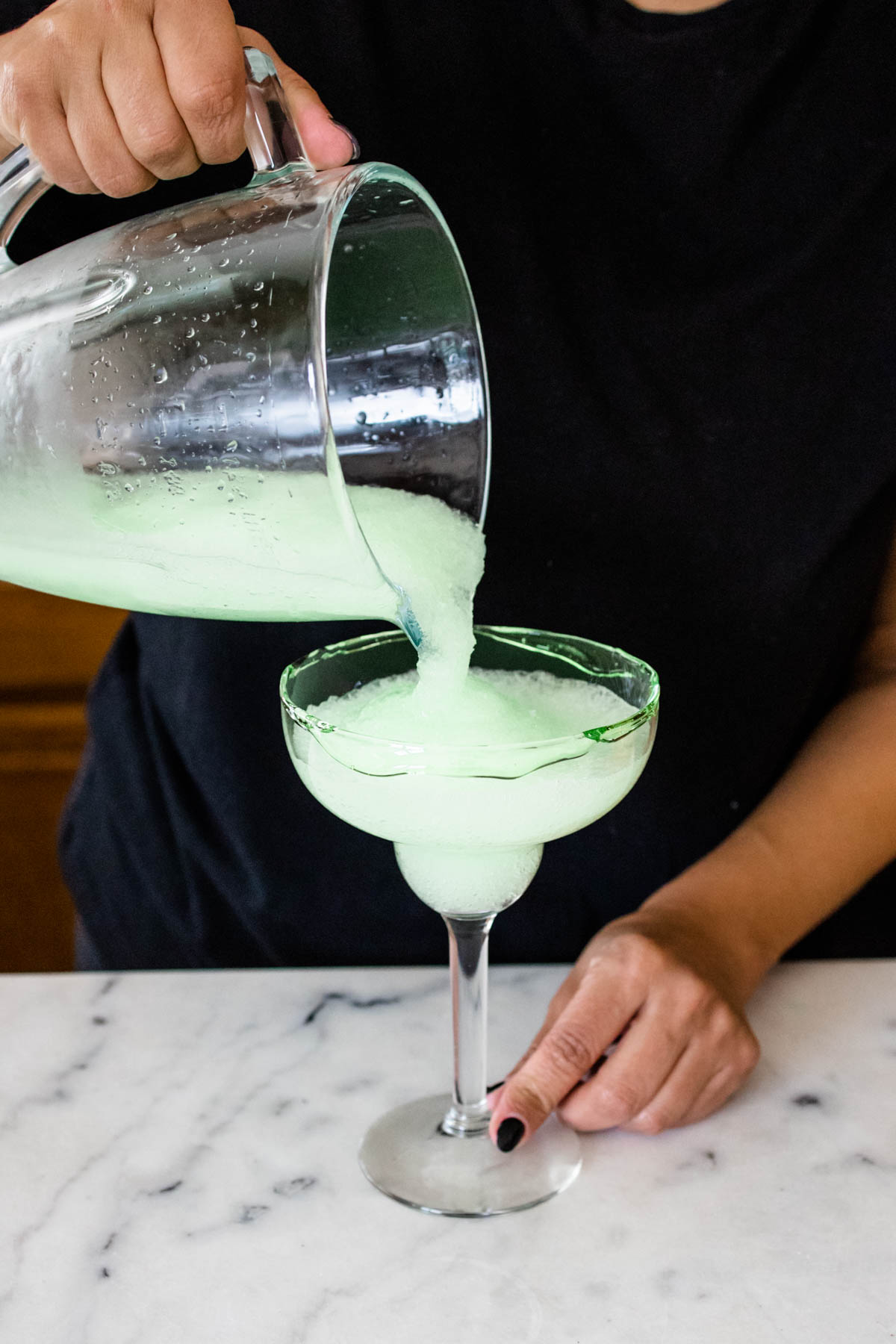 Woman pouring a frozen green Ghostbusters margarita into a margarita glass.