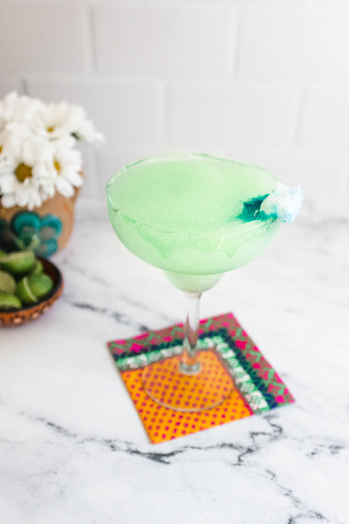 A margarita glass on a table holding a green frozen margarita inspired by the new Ghostbusters movie with a blue melting garnish.