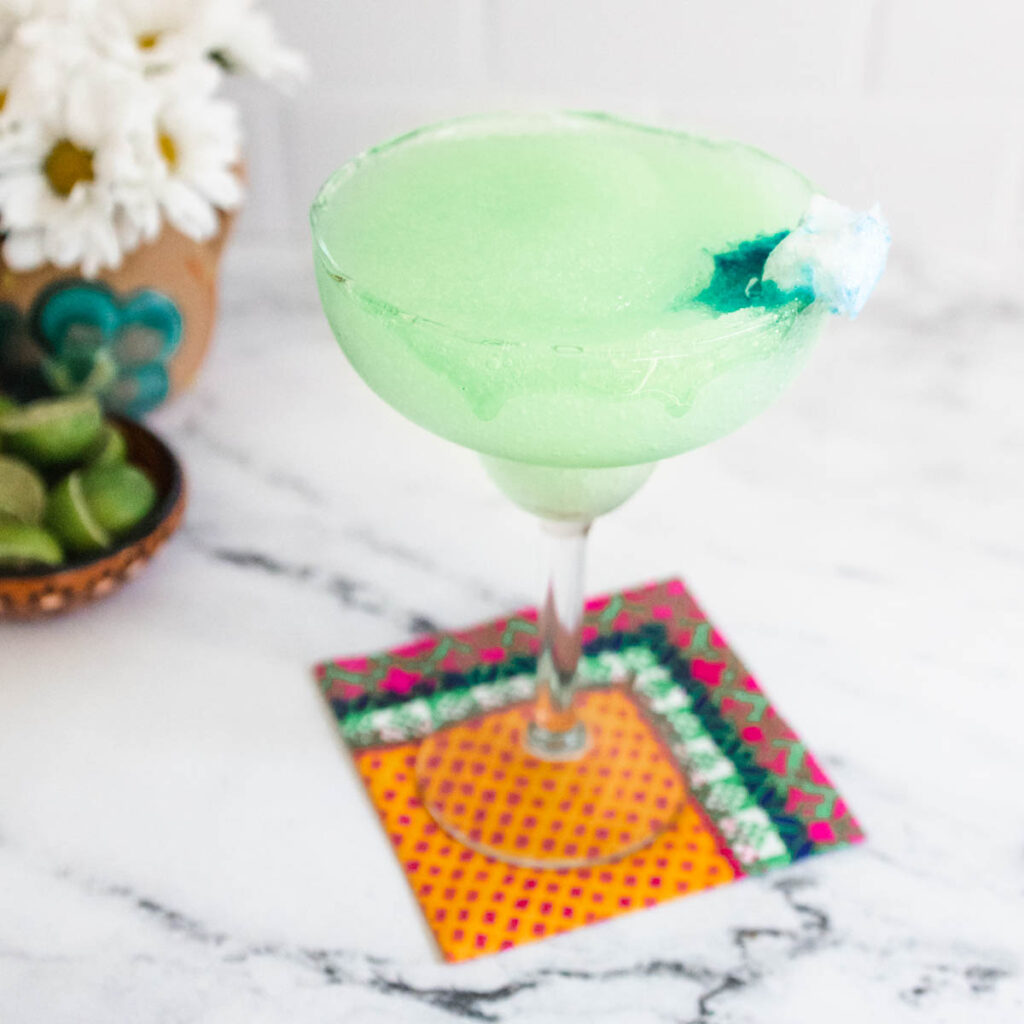 A green Ghostbusters margarita in a margarita glass with a green slime candy rim and blue melting garnish.
