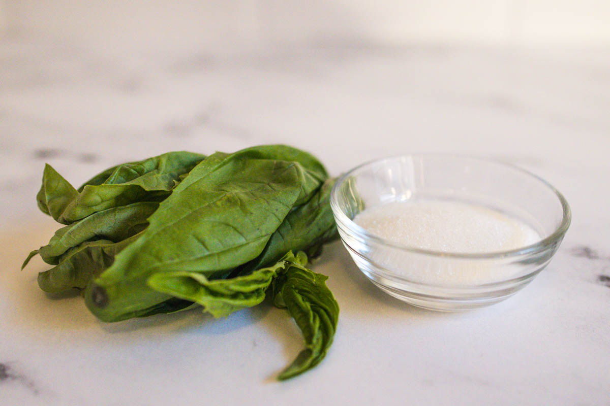 Basil and a small bowl of sugar on a table.