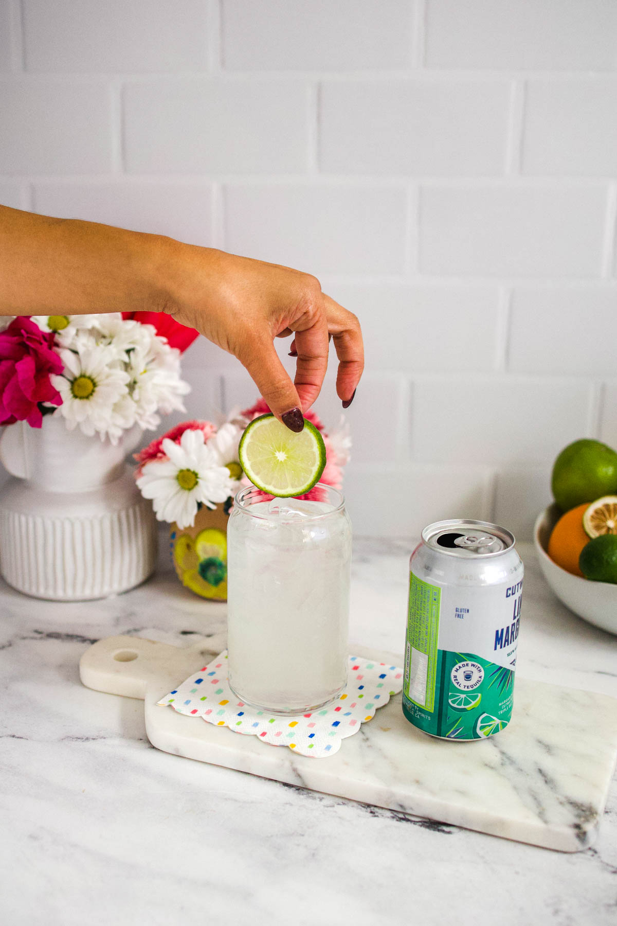 A woman's hand adding a lime wheel to a glass of Cutwater Tequila Margarita next to a can of the cocktail.