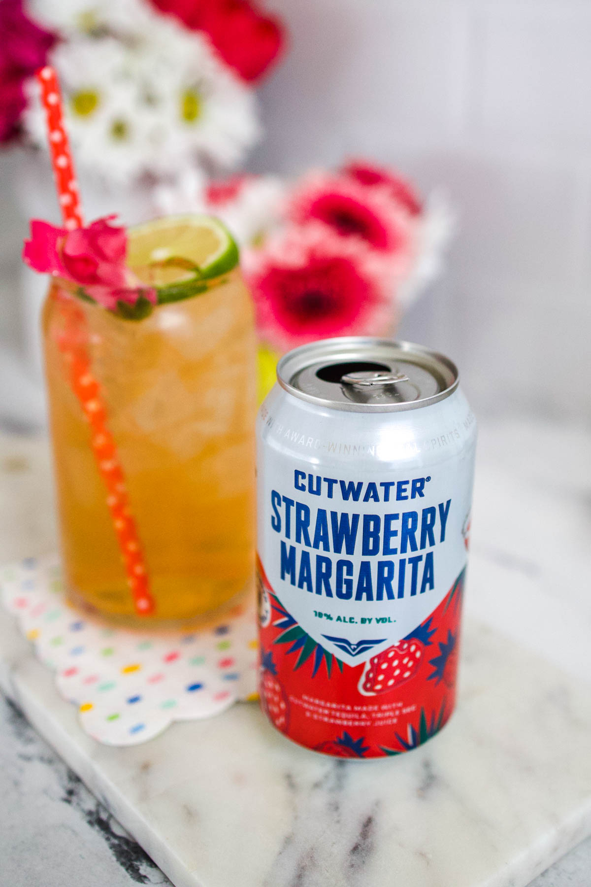 Can of Cutwater Strawberry Margarita on a table with a glass holding the cocktail behind it.