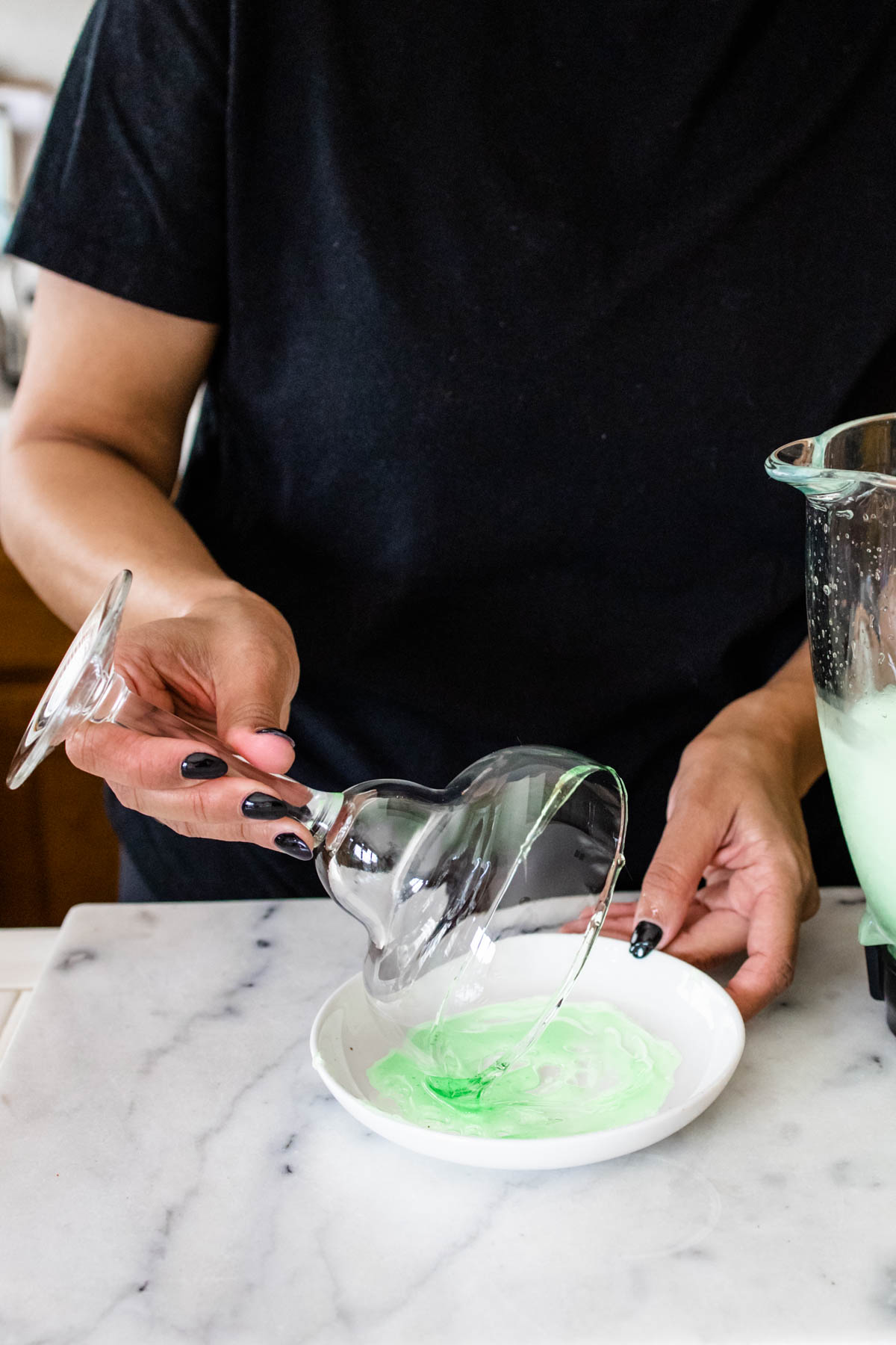 Woman dipping the rim of a margarita glass in green slime candy on a small white plate.