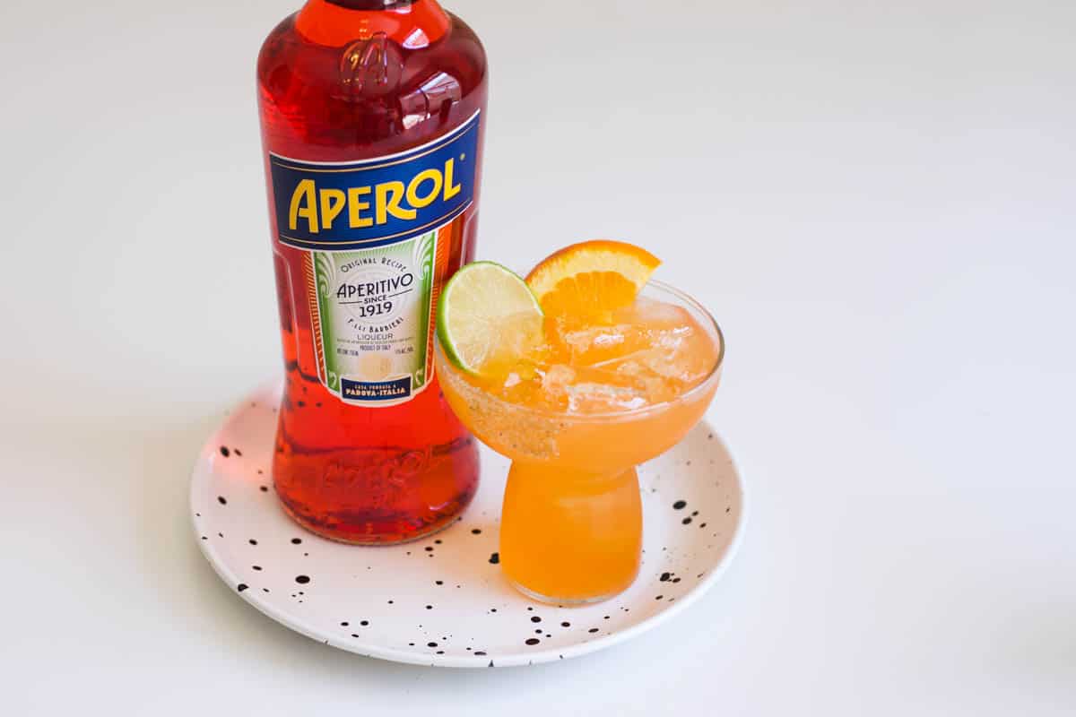A bright orange Aperol margarita served over ice in a glass with spiced sugar rim. 
