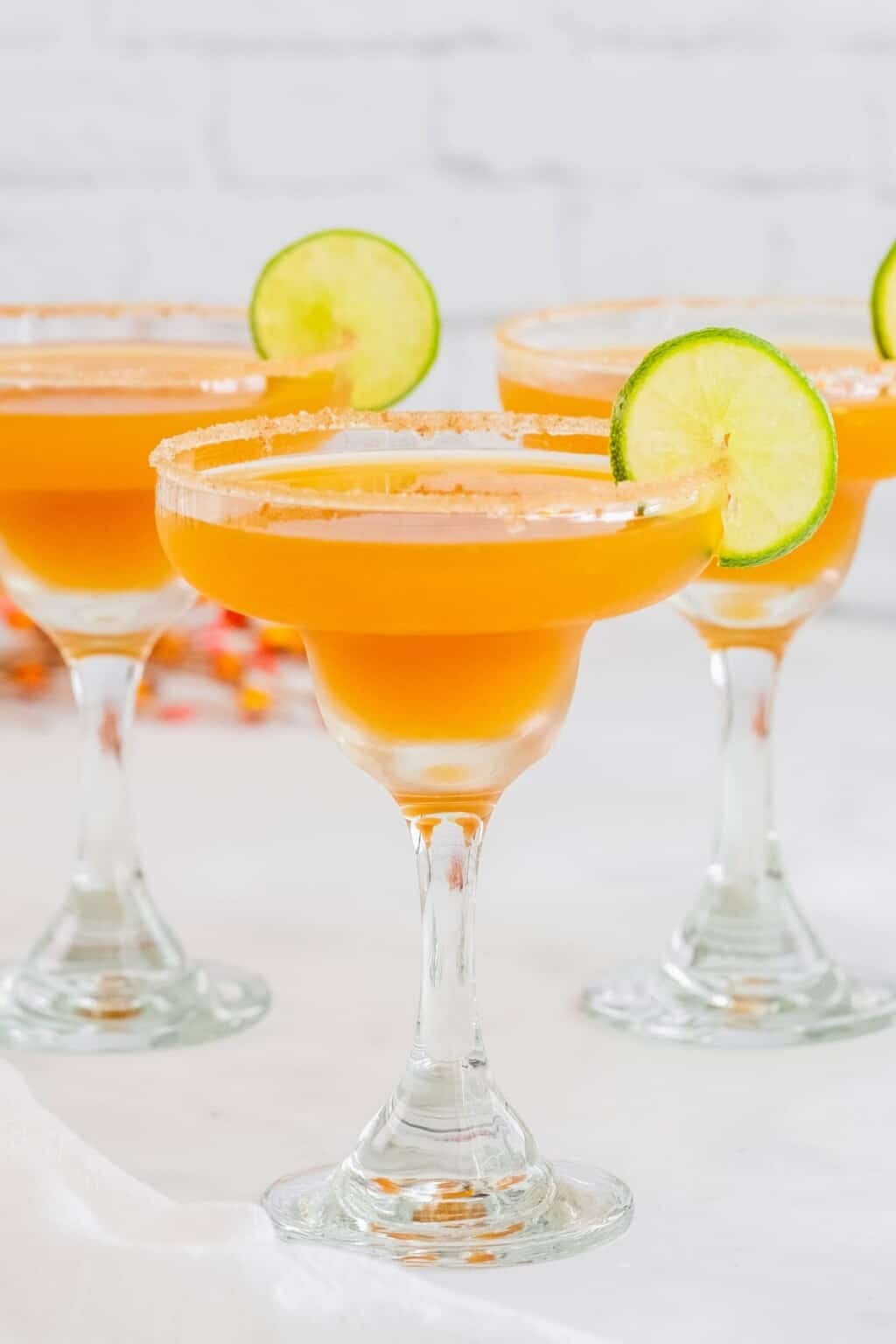 A bright orange margarita served in a margarita glass with lime wedge and a cinnamon and sugar rim. 