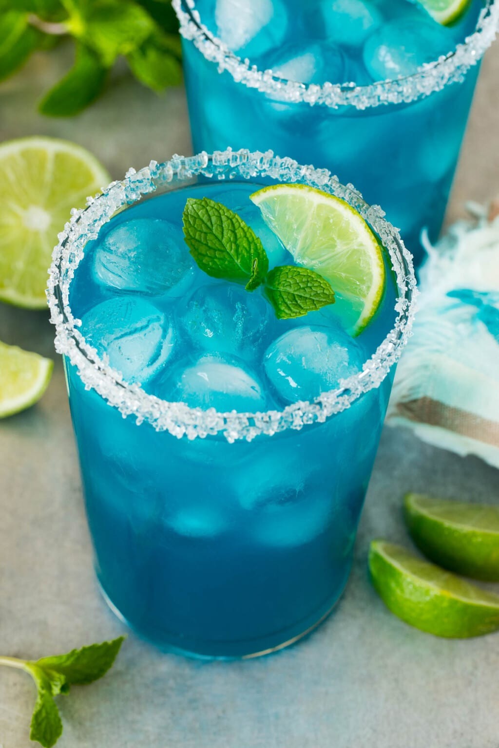 A bright blue margarita served over ice, mint leaves, and lime wedge in a glass with a salt rim.  