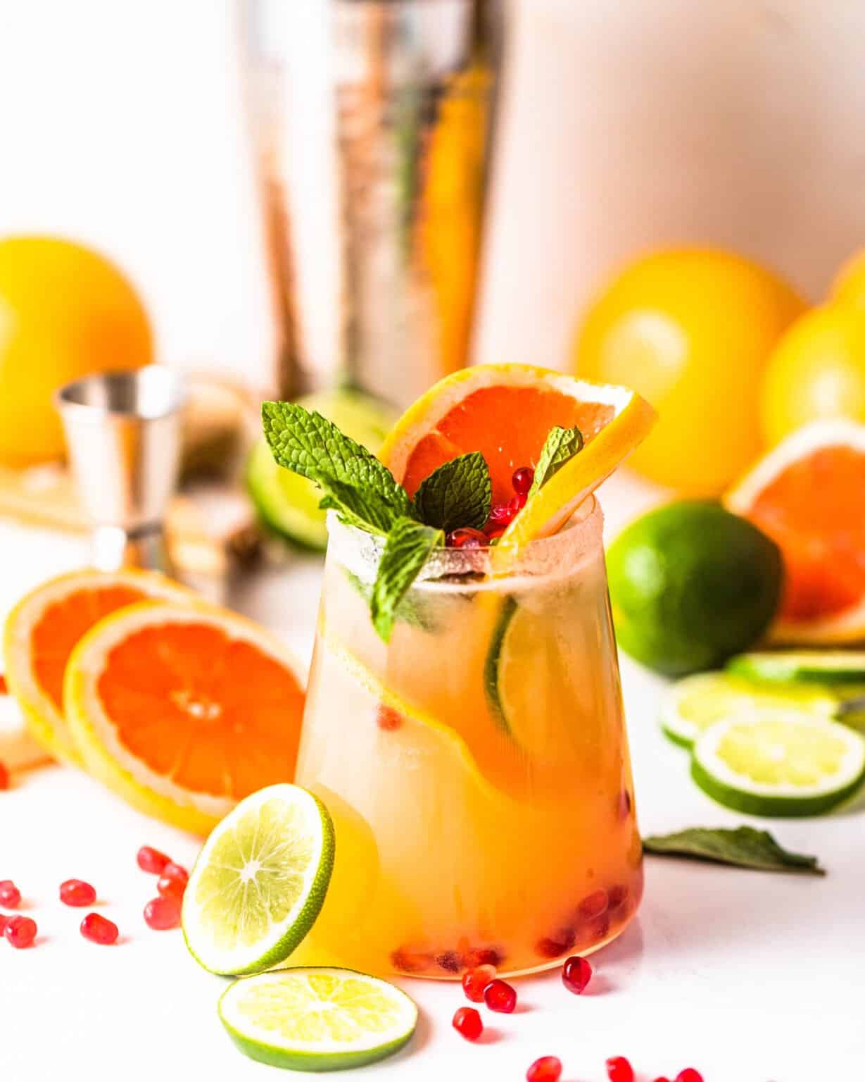 A grapefruit margarita served with grapefruit, limes, pomegranate arils, and mint leaves in a glass with sugar rim. 