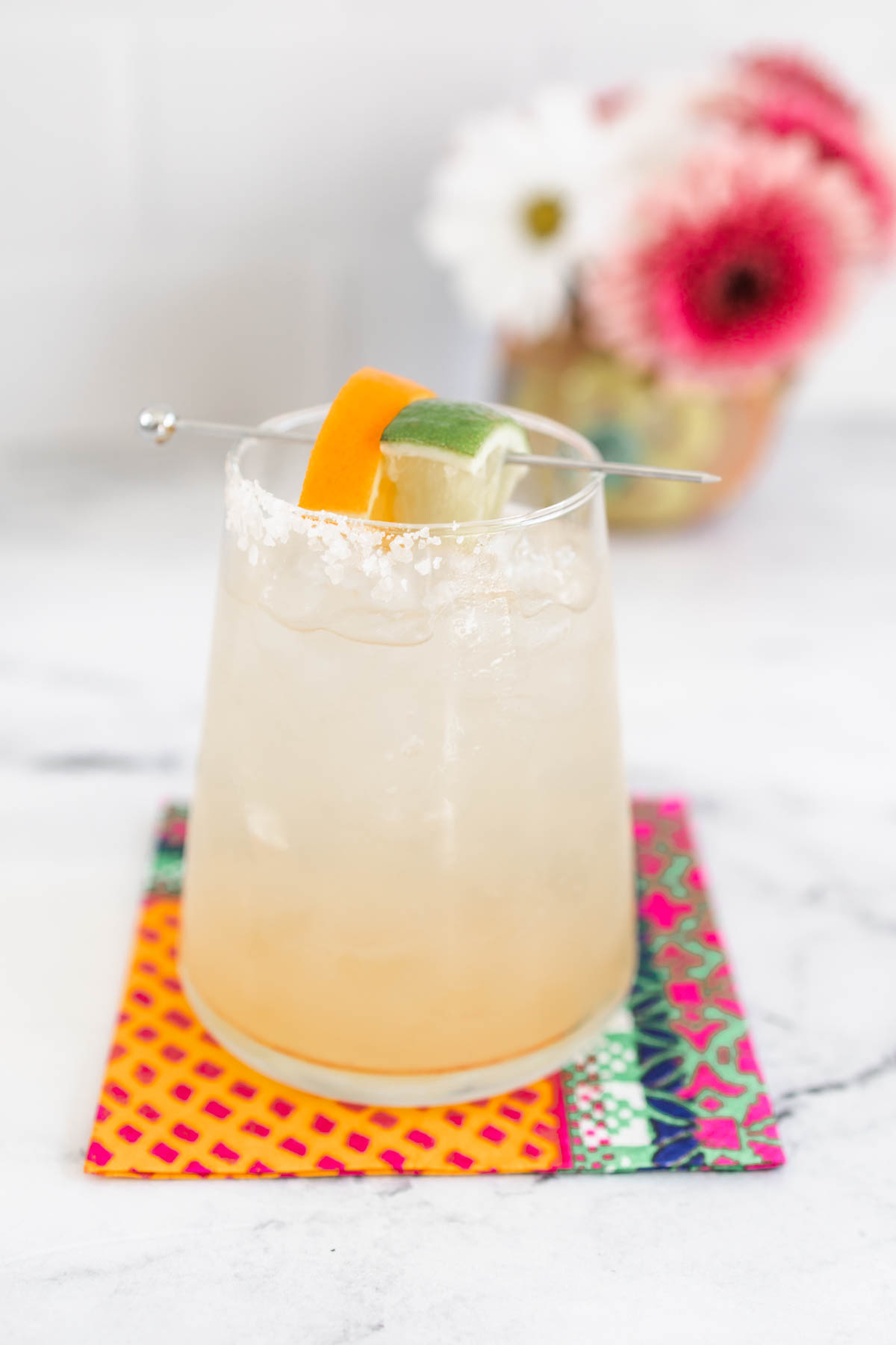 A skinny margarita with orange and lime wedges served in a glass with salt rim.
