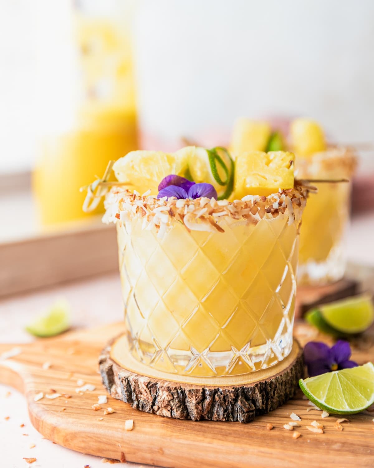 A pina colada margarita served in glass with a toasted coconut rim and with pineapple and lime slices on a stick on top.  