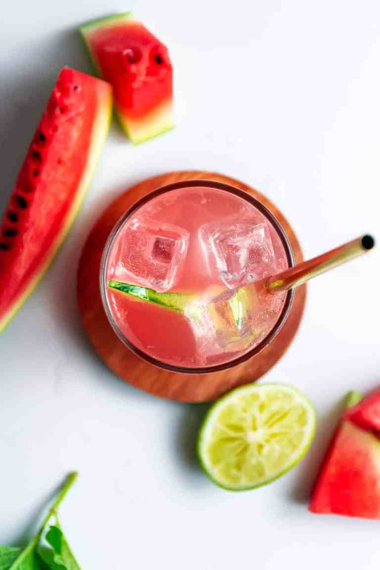 A bright red watermelon margarita served with ice cubes, lime wedge, and a metal straw. 