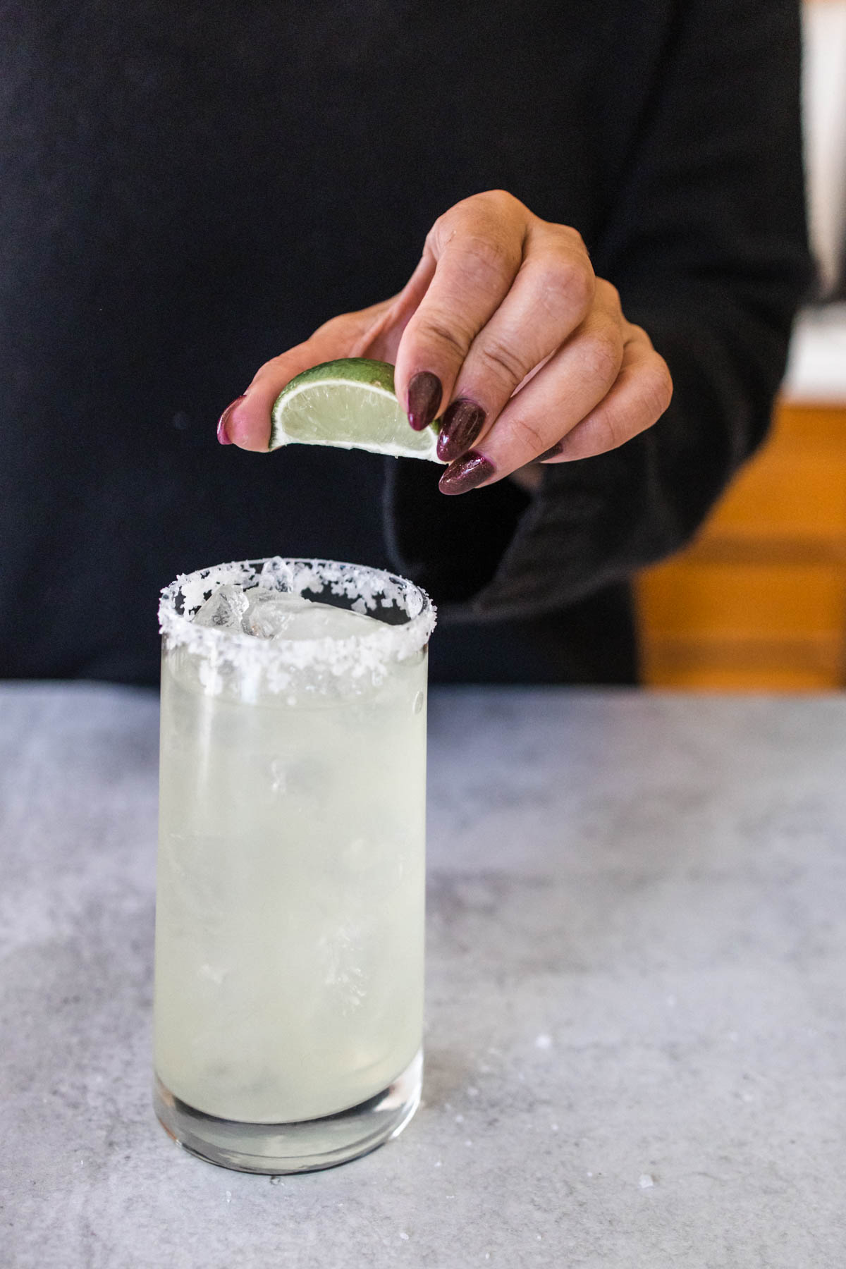 A woman squeezing a lime over a glass of margarita with salt rim.