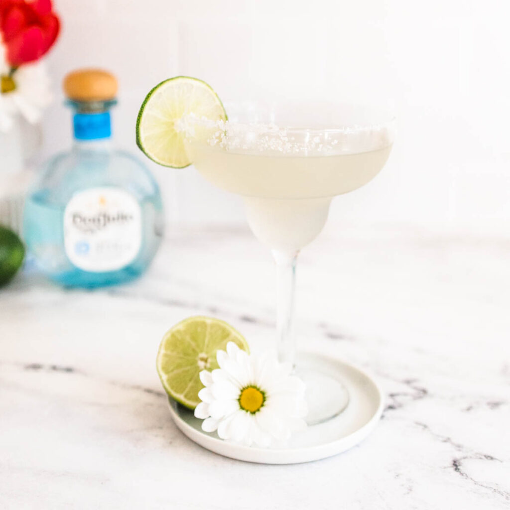 Classic lime margarita on a plate with a daisy and half a lime.