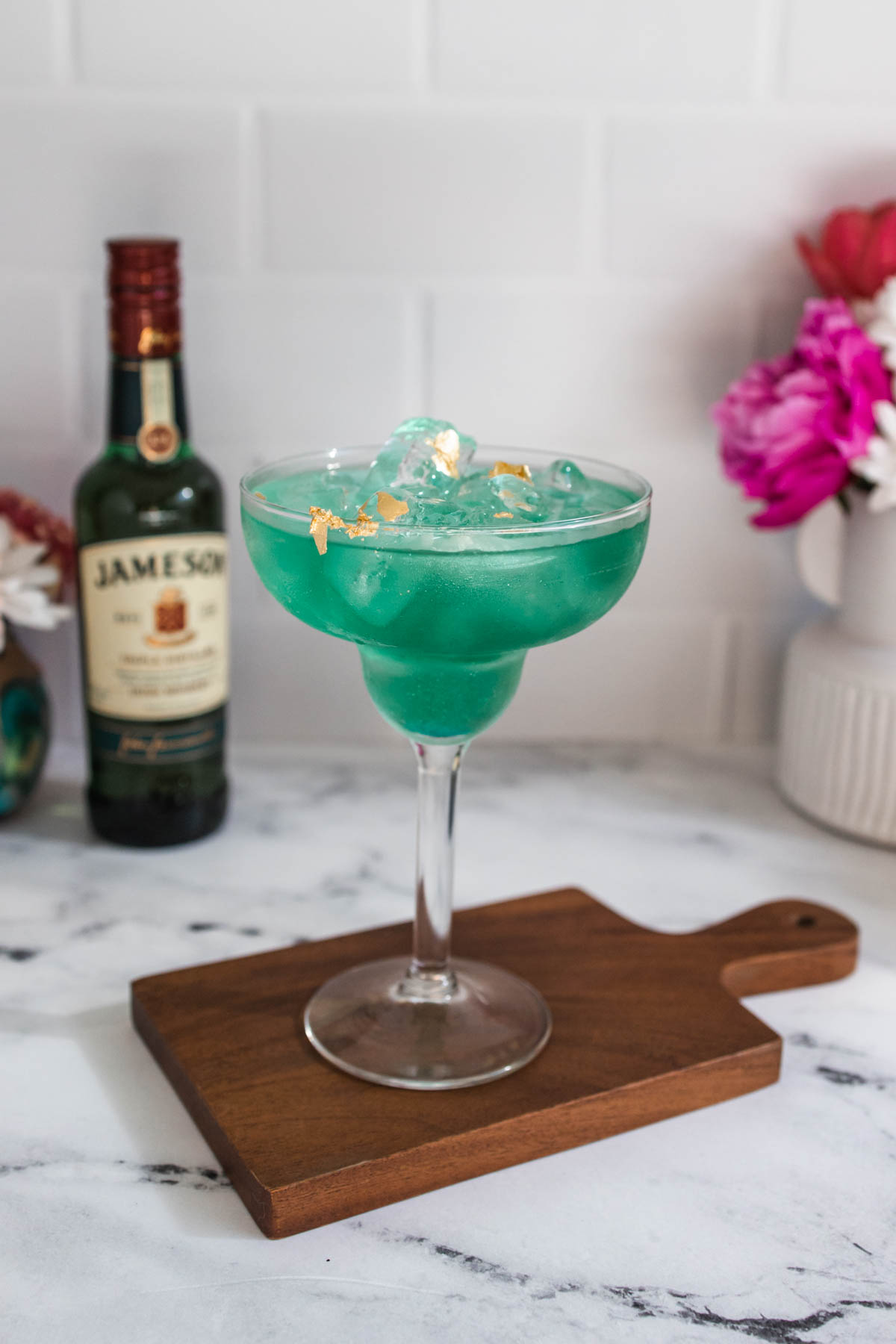 A green Irish Margarita for St. Patrick's Day on a wood tray with a bottle of Jameson Irish Whiskey behind it.