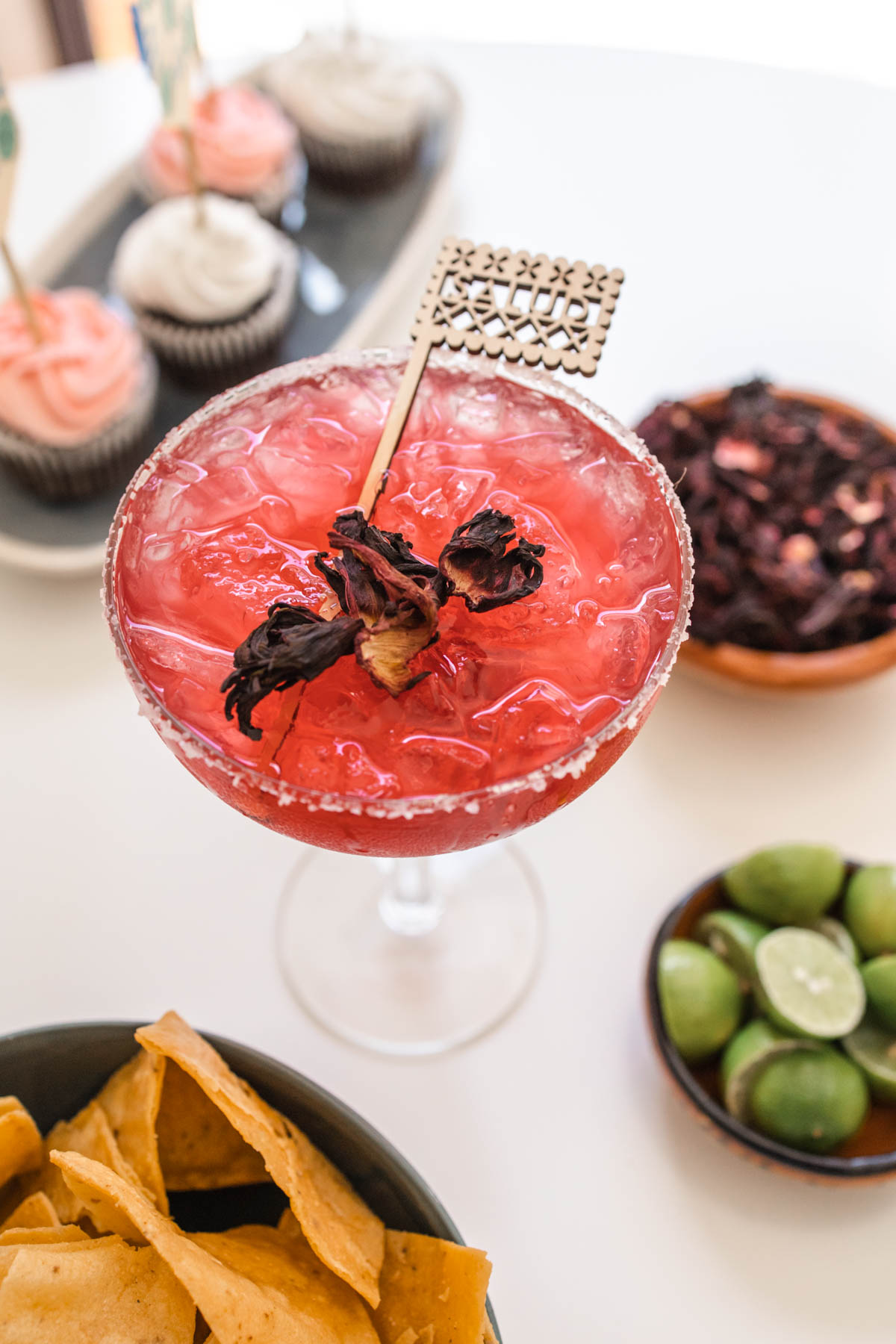 Close up of a Hibiscus Margarita with dried Hibiscus leaves and a papel picado stir stick.