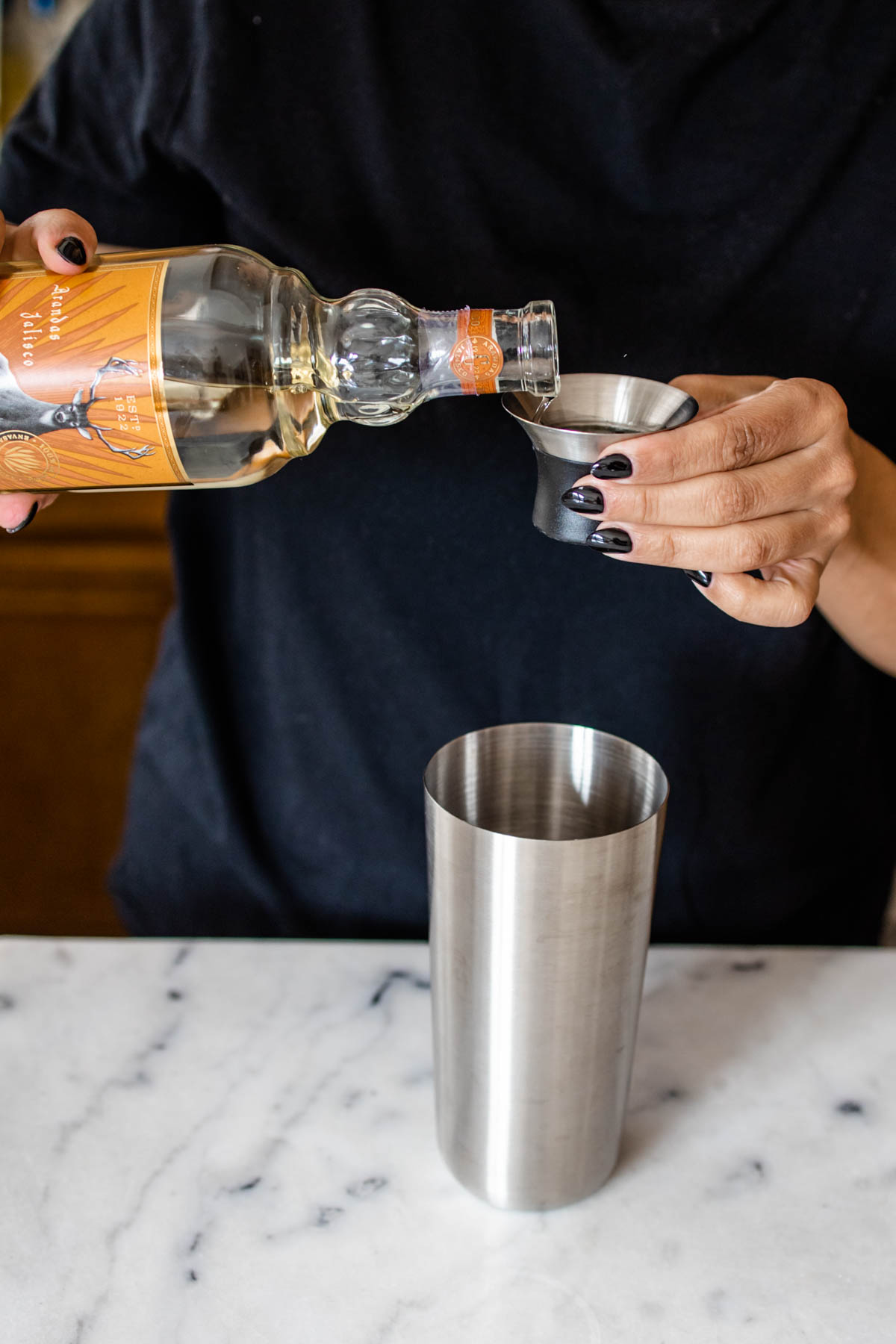 A woman pouring Triple Sec into a jigger before adding it into the shaker.