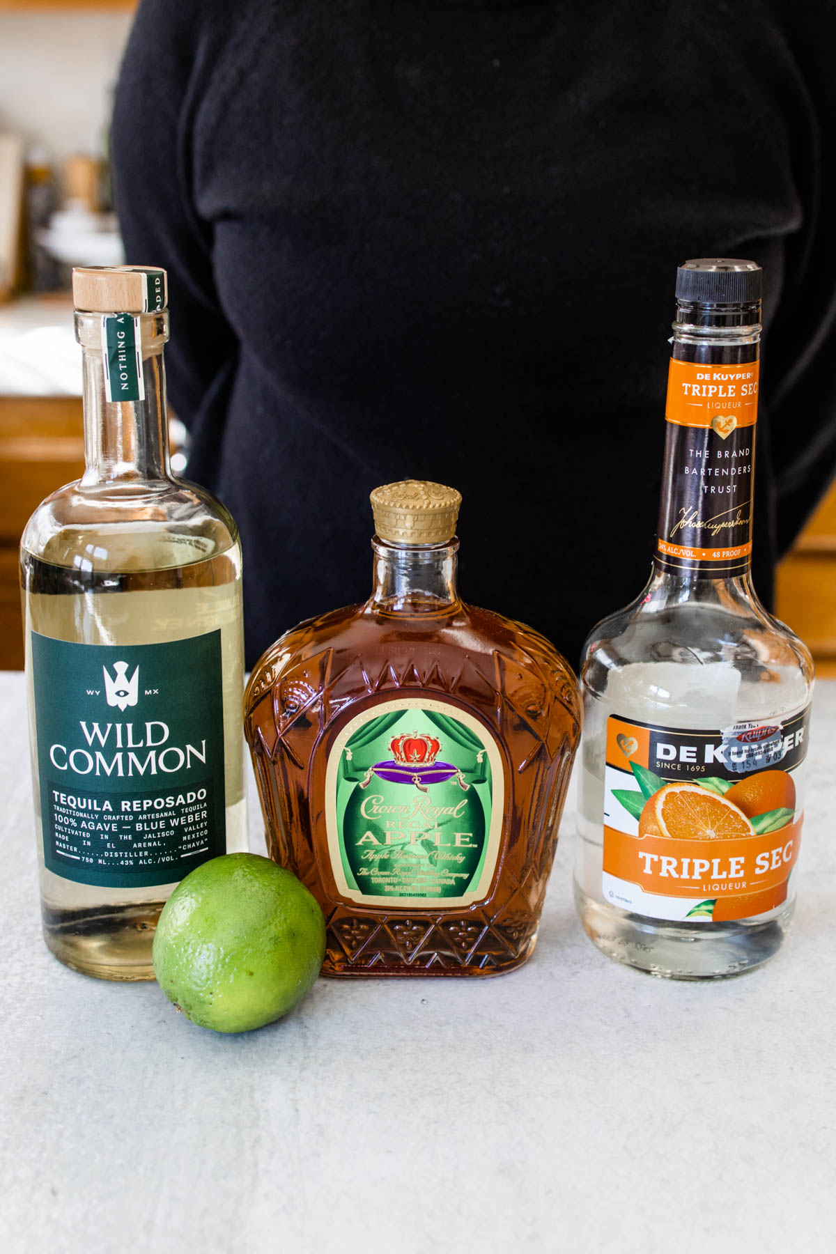 A bottle of Wild Common Tequila Reposado, Crown Royal Regal Apple Whiskey, Triple Sec, and fresh lime.