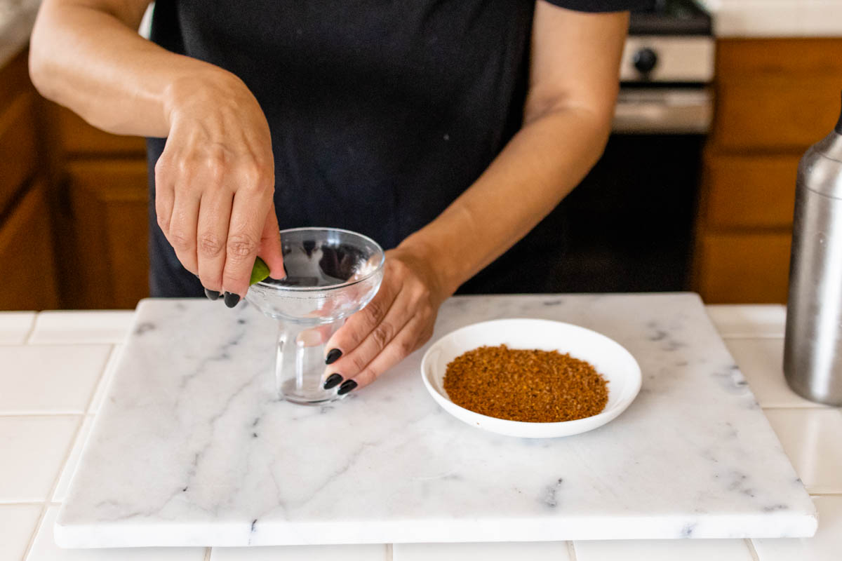 Woman rubbing a lime on the edge of a margarita glass to rim it with tajin.