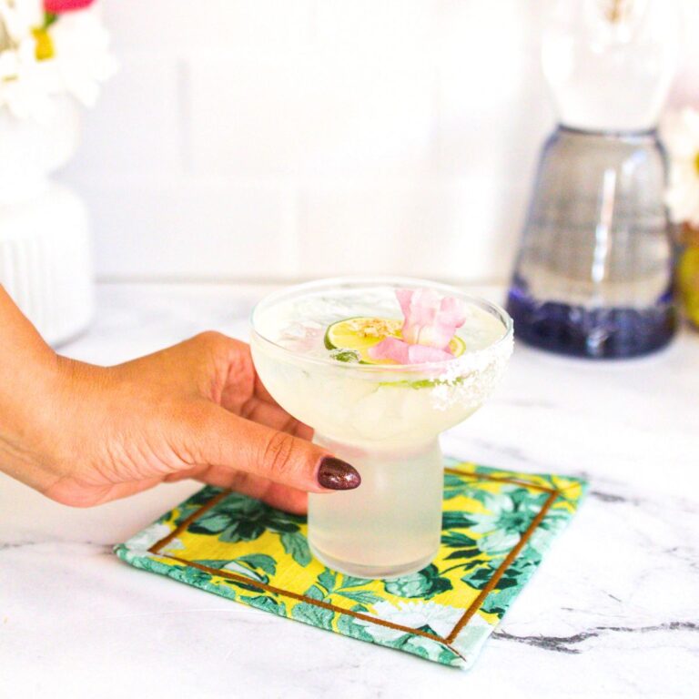 A beautiful glass of Clase Azul margarita with salted rim and garnished with a lime wheel, edible gold leaves, and flowers.