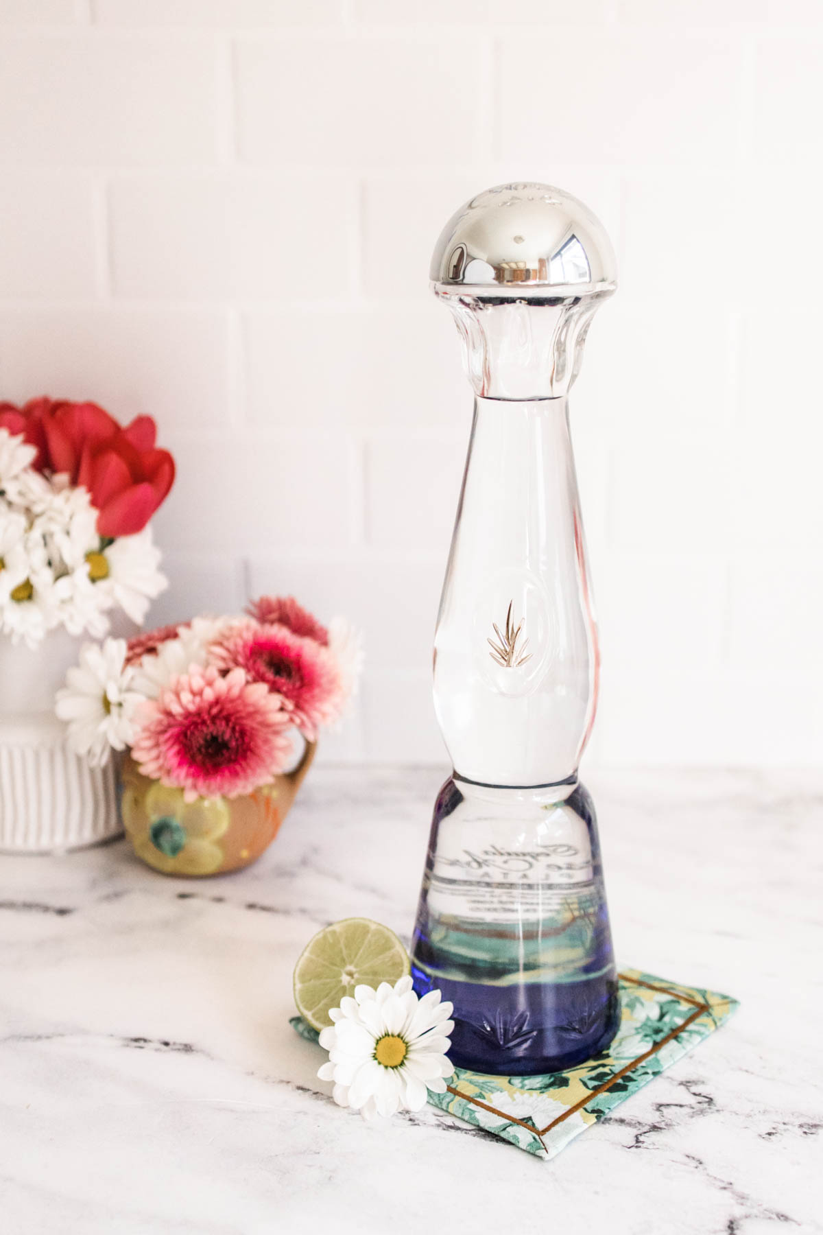 A beautiful bottle of Clase Azul Tequila Plata with decorative flowers in the background.