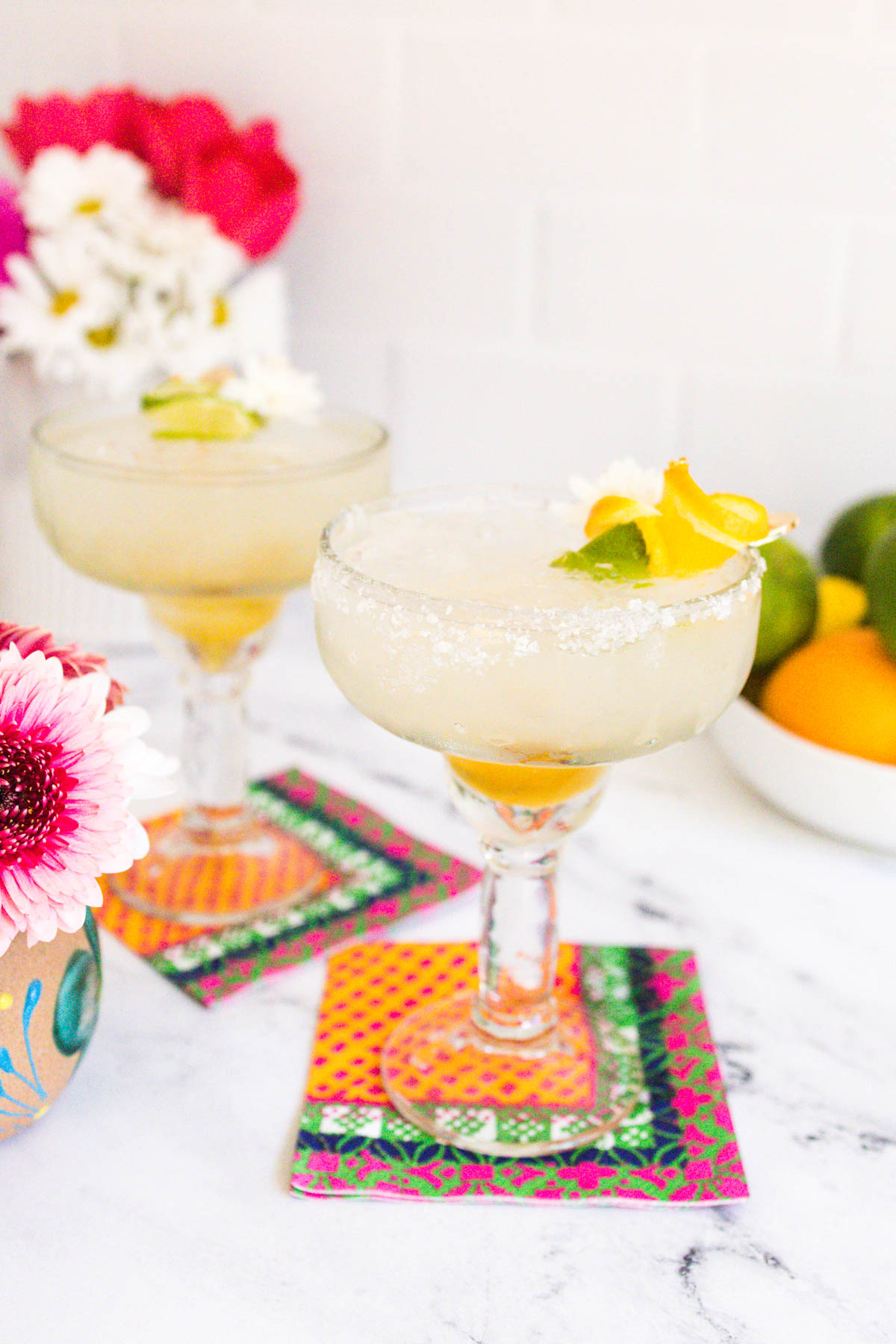 Two glasses of golden Cadillac Margaritas with with lime wedges as garnish.