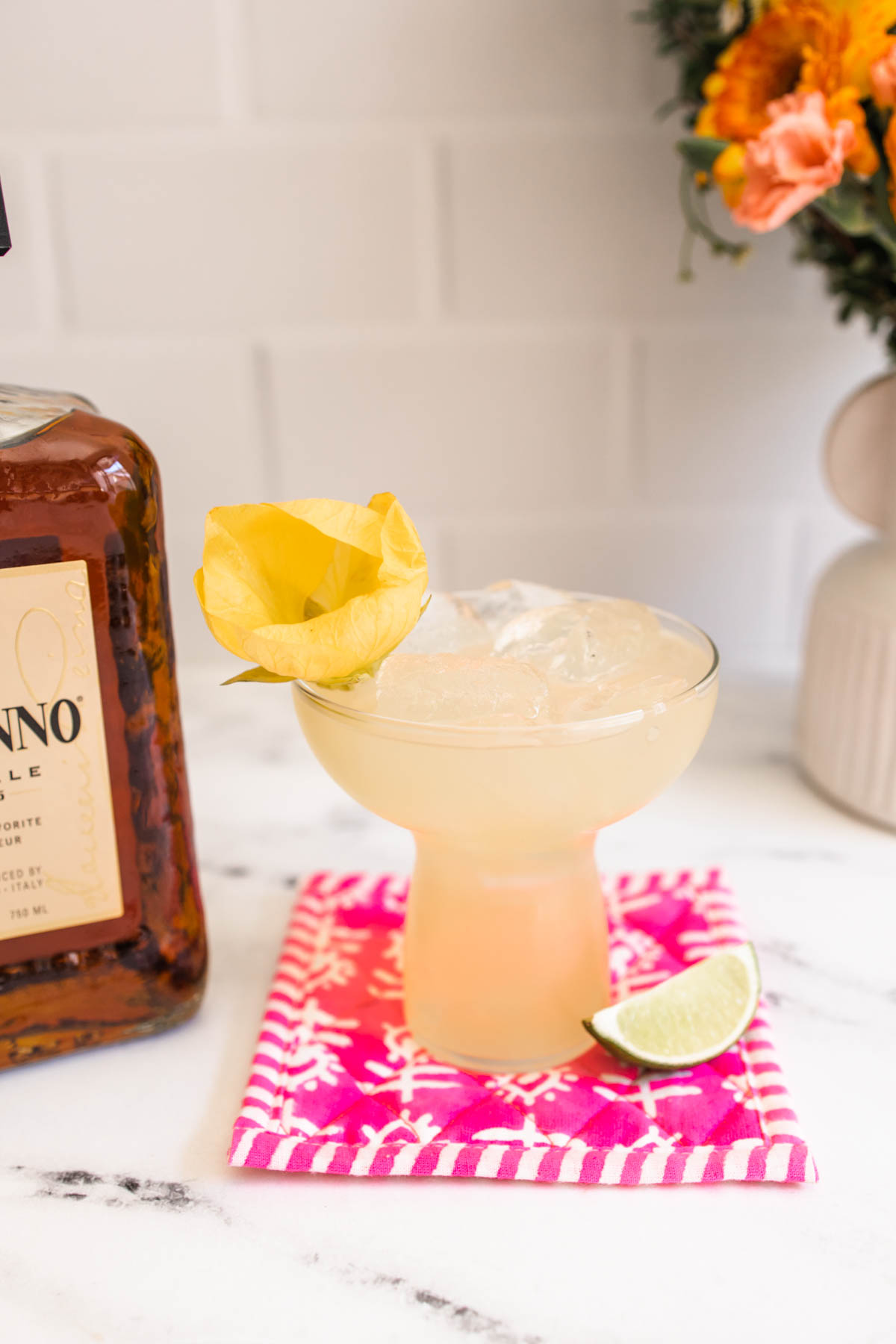 A glass of Disaronno margarita with a yellow flower garnish. in front of a Disaronno Amaretto bottle.