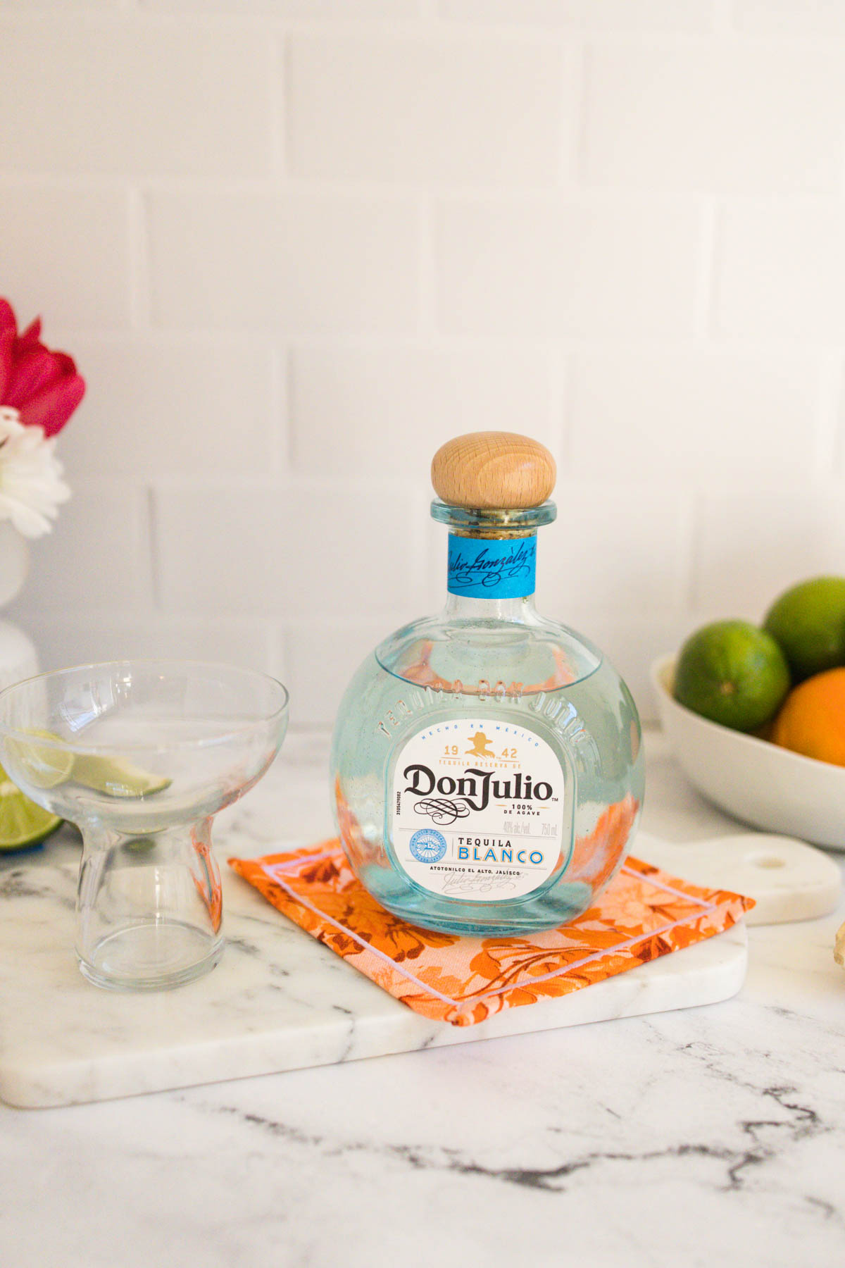 A bottle of Don Julio Blanco Tequila alongside a stemless margarita glass on a marble counter.
