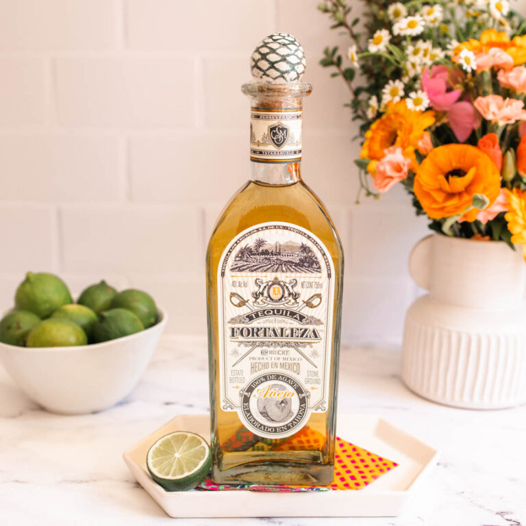 A clear bottle of Fortaleza Tequila Anejo on top of a colored napkin beside a halved lime.