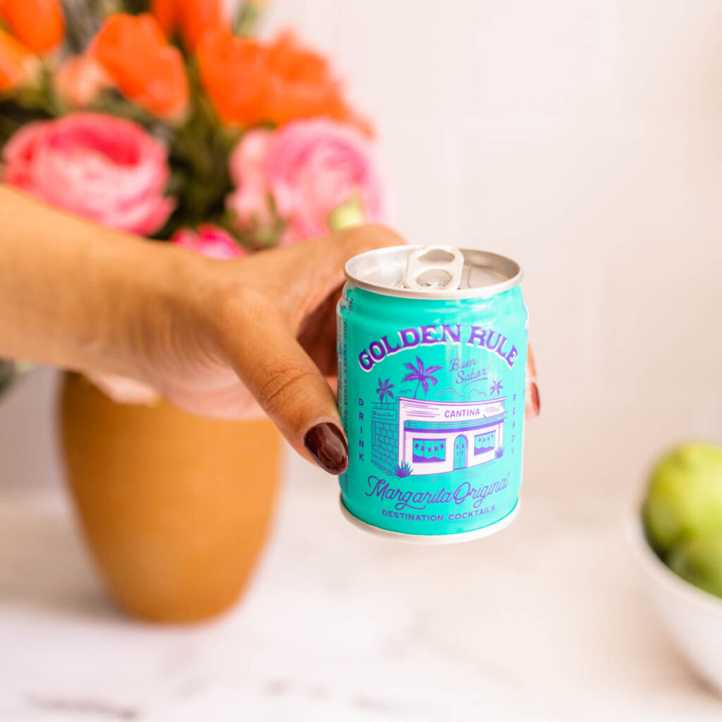 A hand holding the pretty can of Golden Rule Margarita.