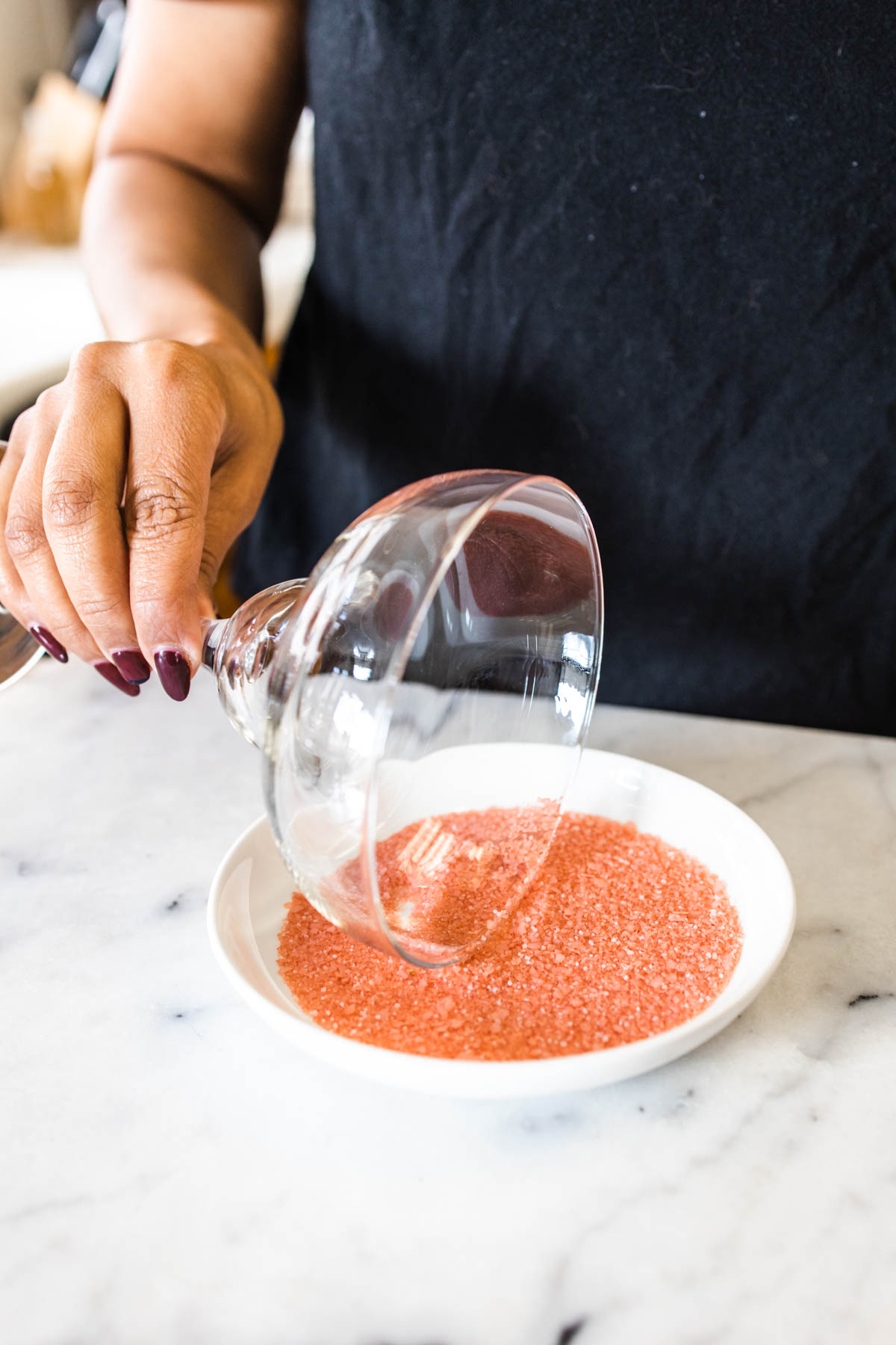 A woman dipping a portion of the margarita glass on a small plate with grapefruit-flavored kosher salt.