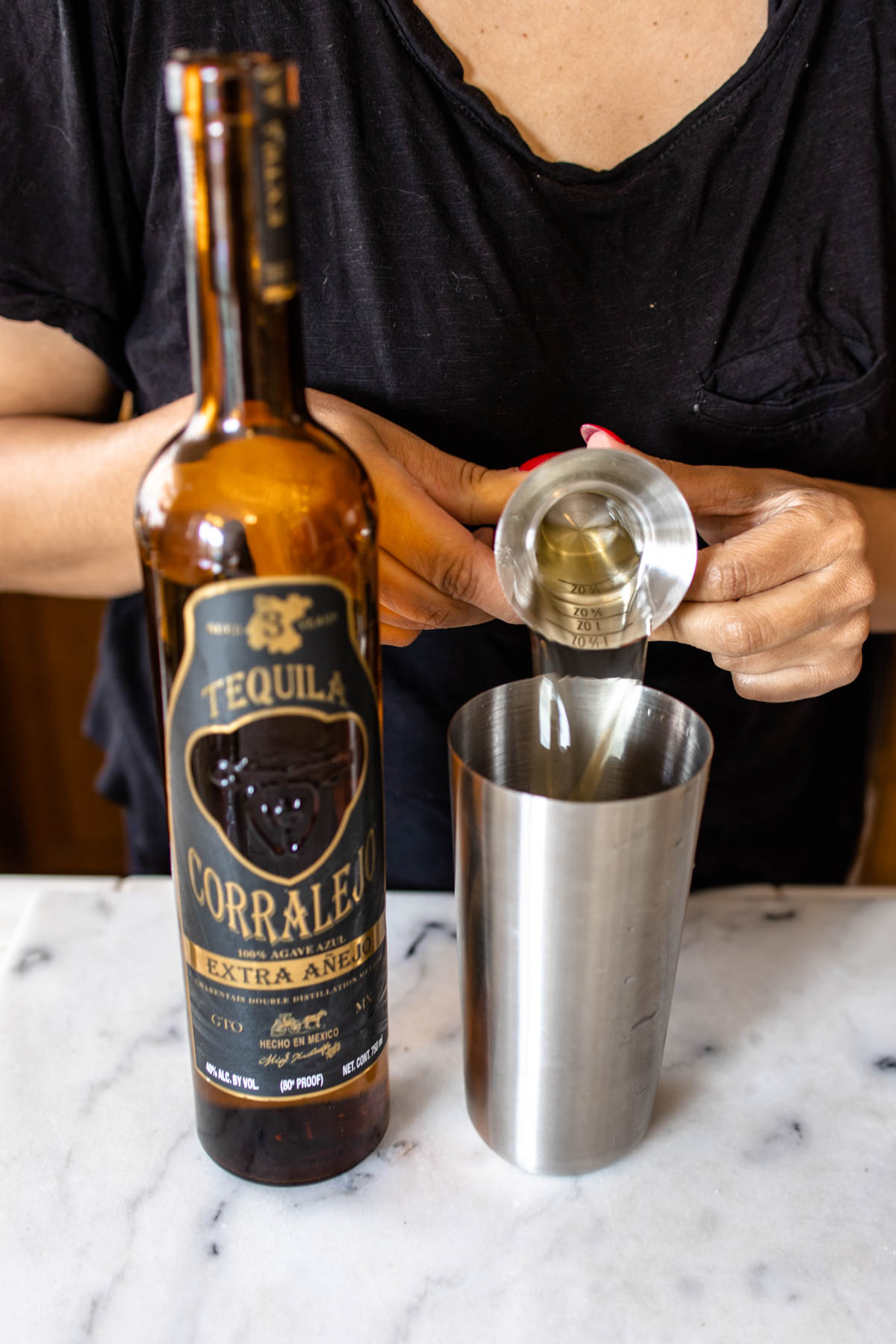 Pouring anejo tequila into a cocktail shaker from a jigger.