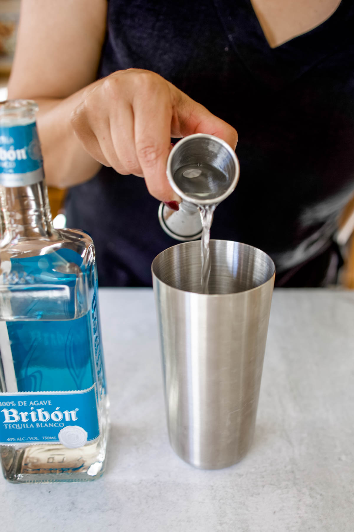 A woman pouring some Bribón Tequila Blanco into the cocktail shaker from a jigger.