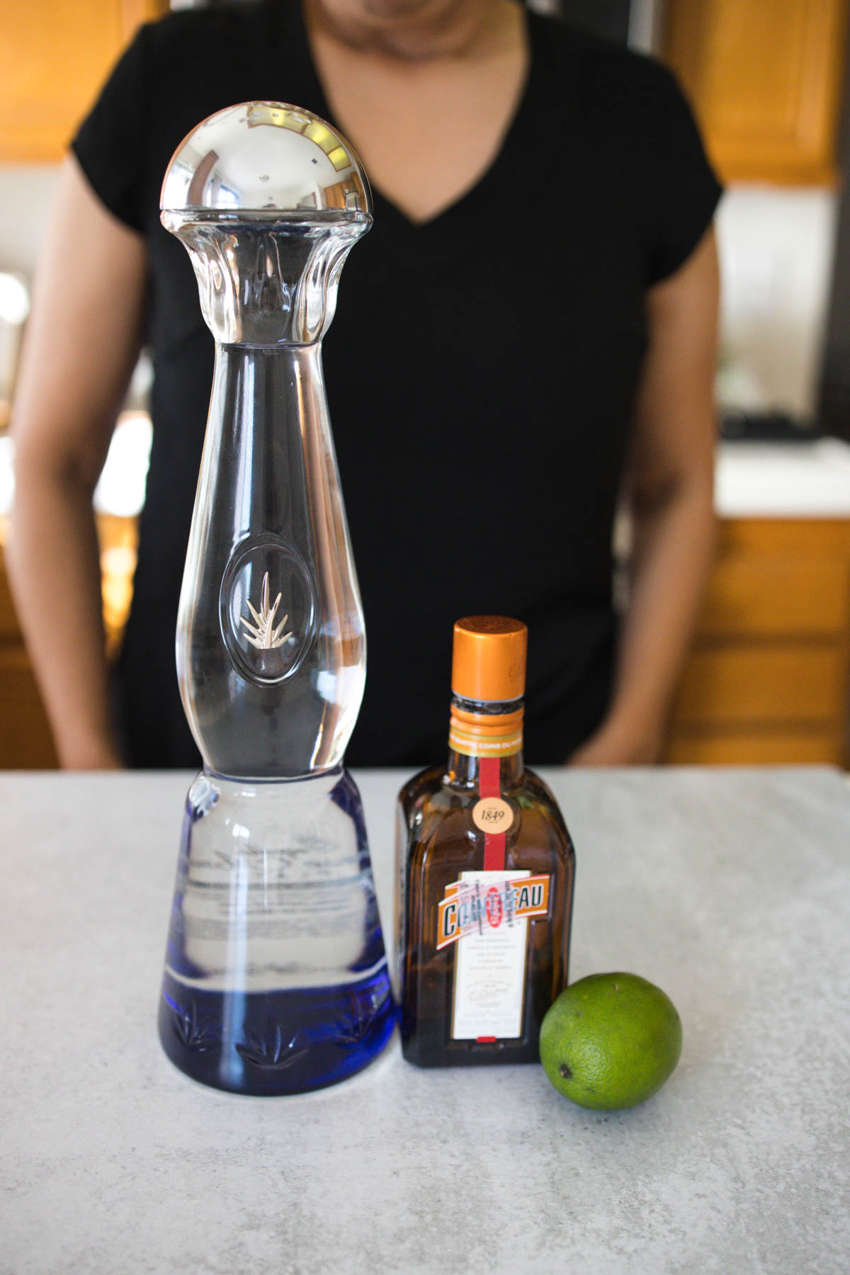 A bottle of Clase Azul Tequila Plata, Cointreau, and fresh lime on top of a counter.