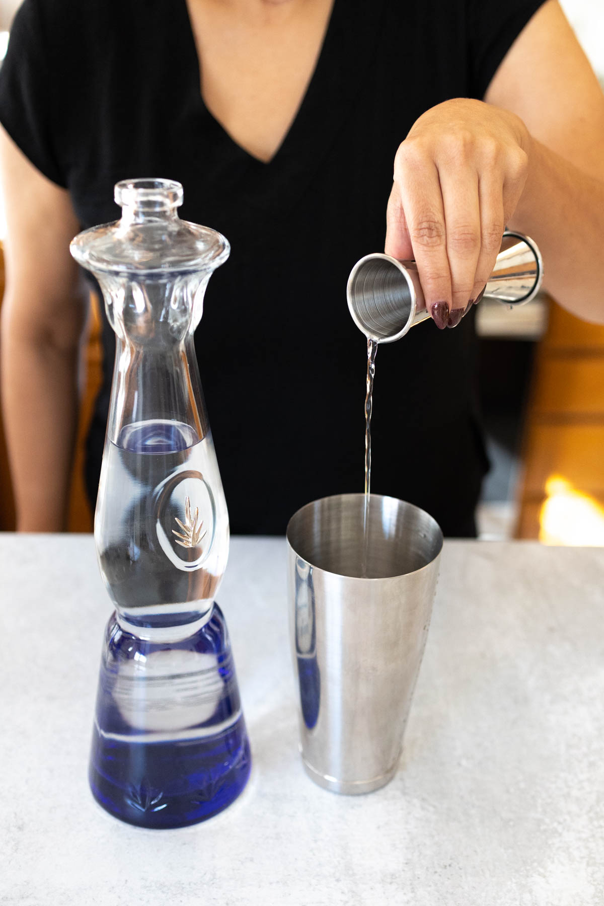 A woman pouring some Clase Azul Tequila Plate from the jigger into a shaker.