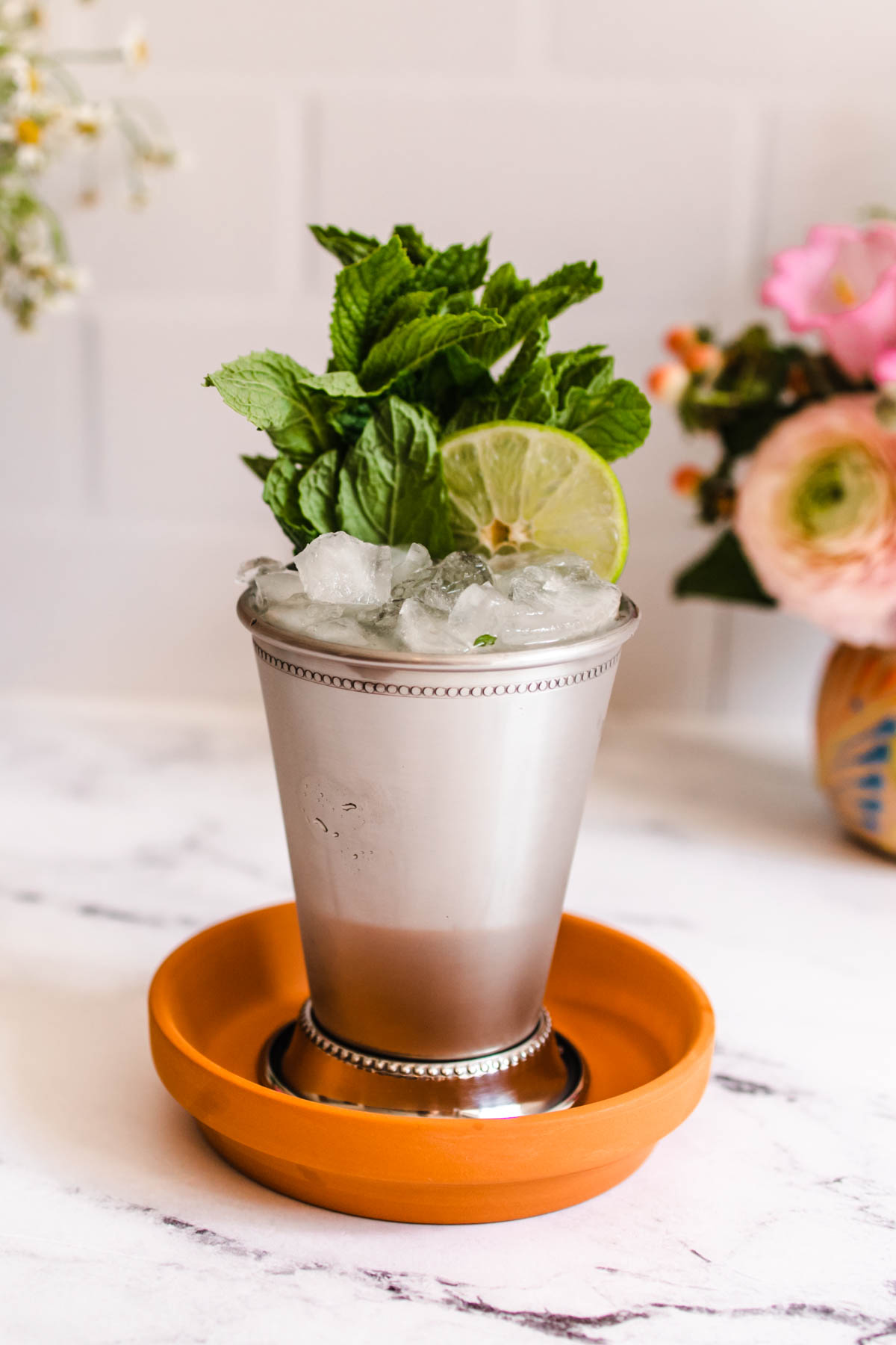 A Mint Julep Margarita in a silver mint Julep cup on a terracotta plate with mint and lime garnish. 