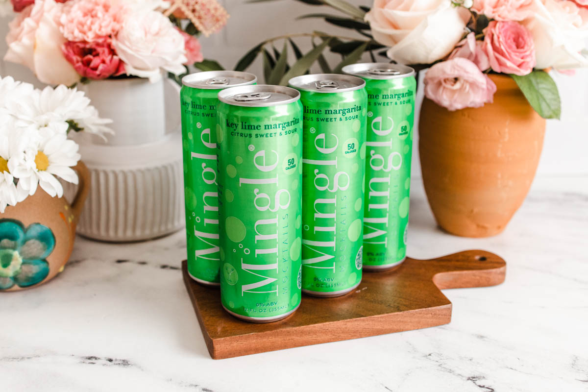 Four green cans of Mingle Mocktails Key Lime Margarita arranged on top of a cutting board.