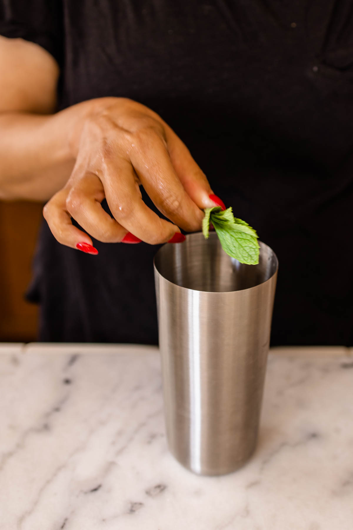 Woman adding fresh mint to a cocktail shaker. 