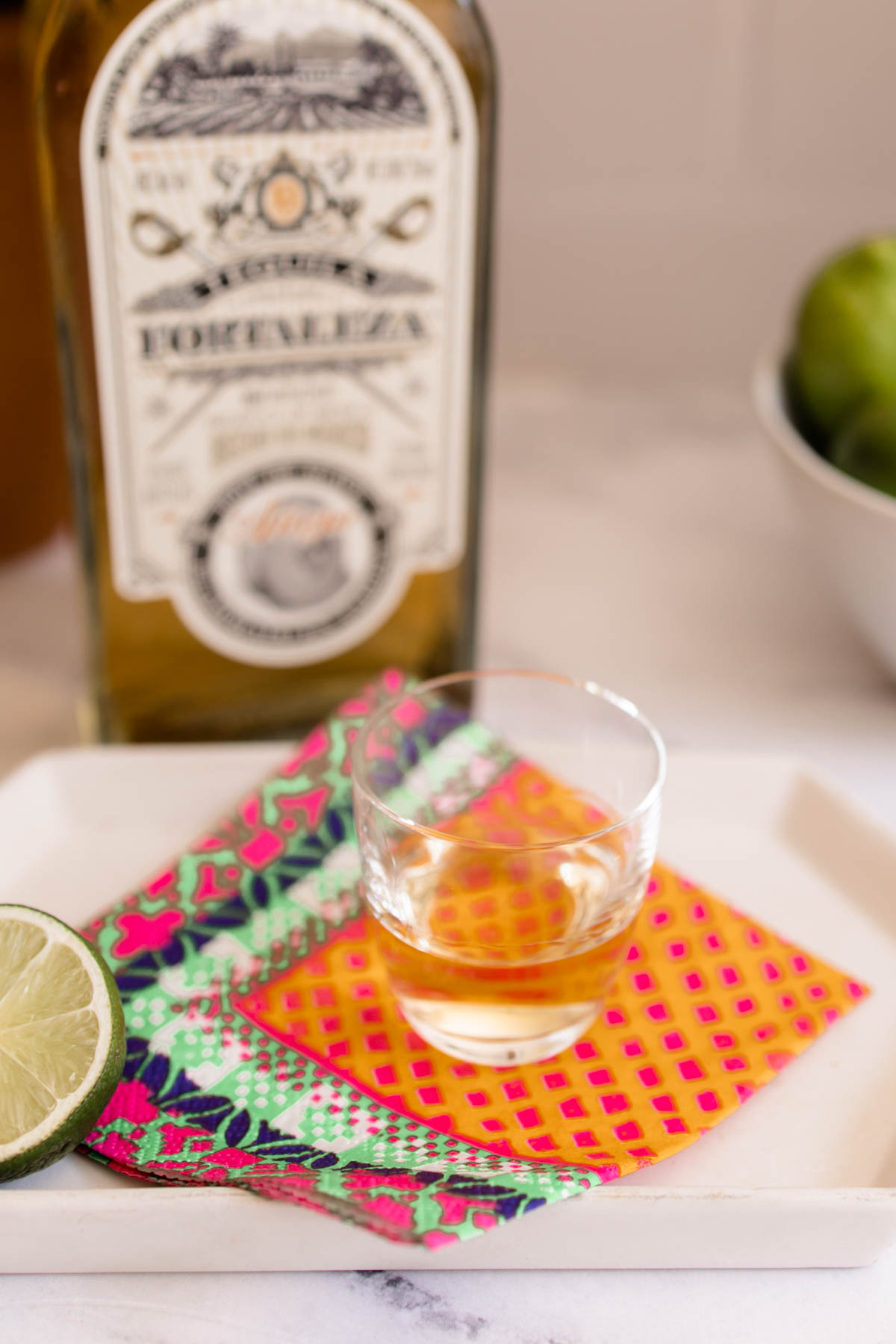 A glass on a colored napkin in front of a bottle of Fortaleza Tequila Anejo.