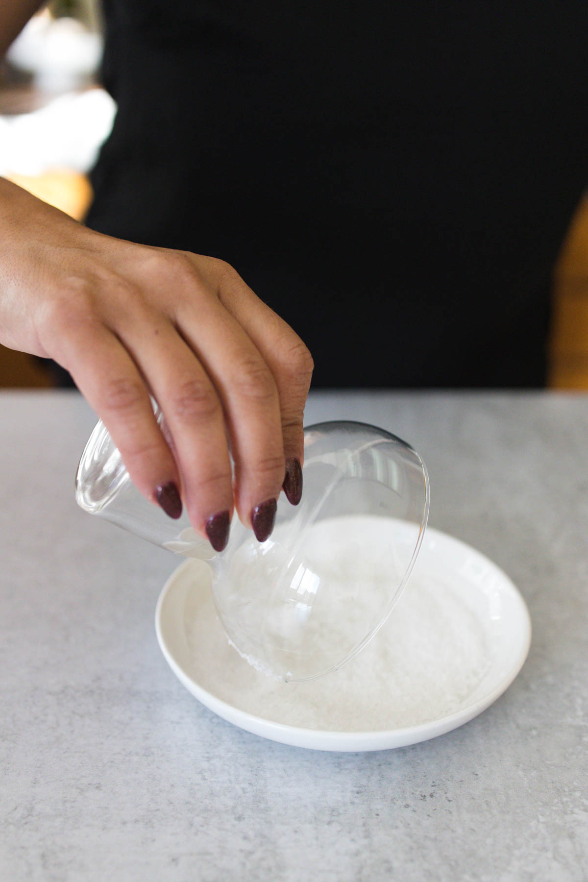 A woman dipping portion of a margarita glass in a small plate with salt.