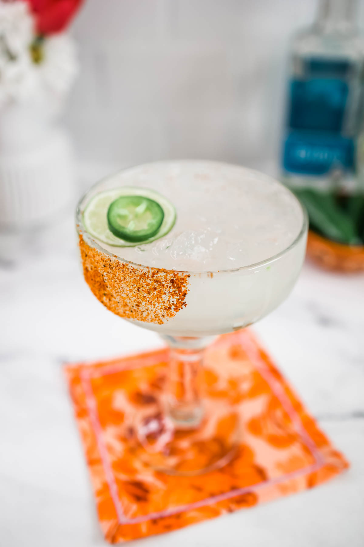 A simple spicy margarita garnished with jalapeno slice and lime wheel inside a margarita glass with Tajin rim.