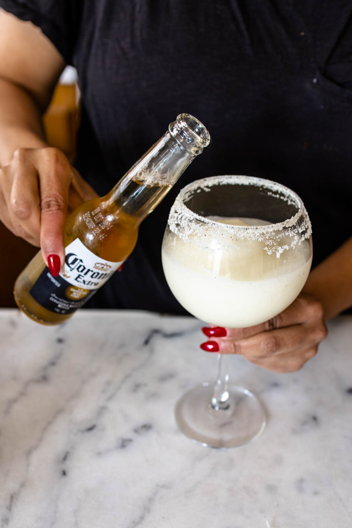 A person about to invert an opened bottle of Corona Light Beer into a Frozen Coronarita in a glass with pickle-flavored rim.