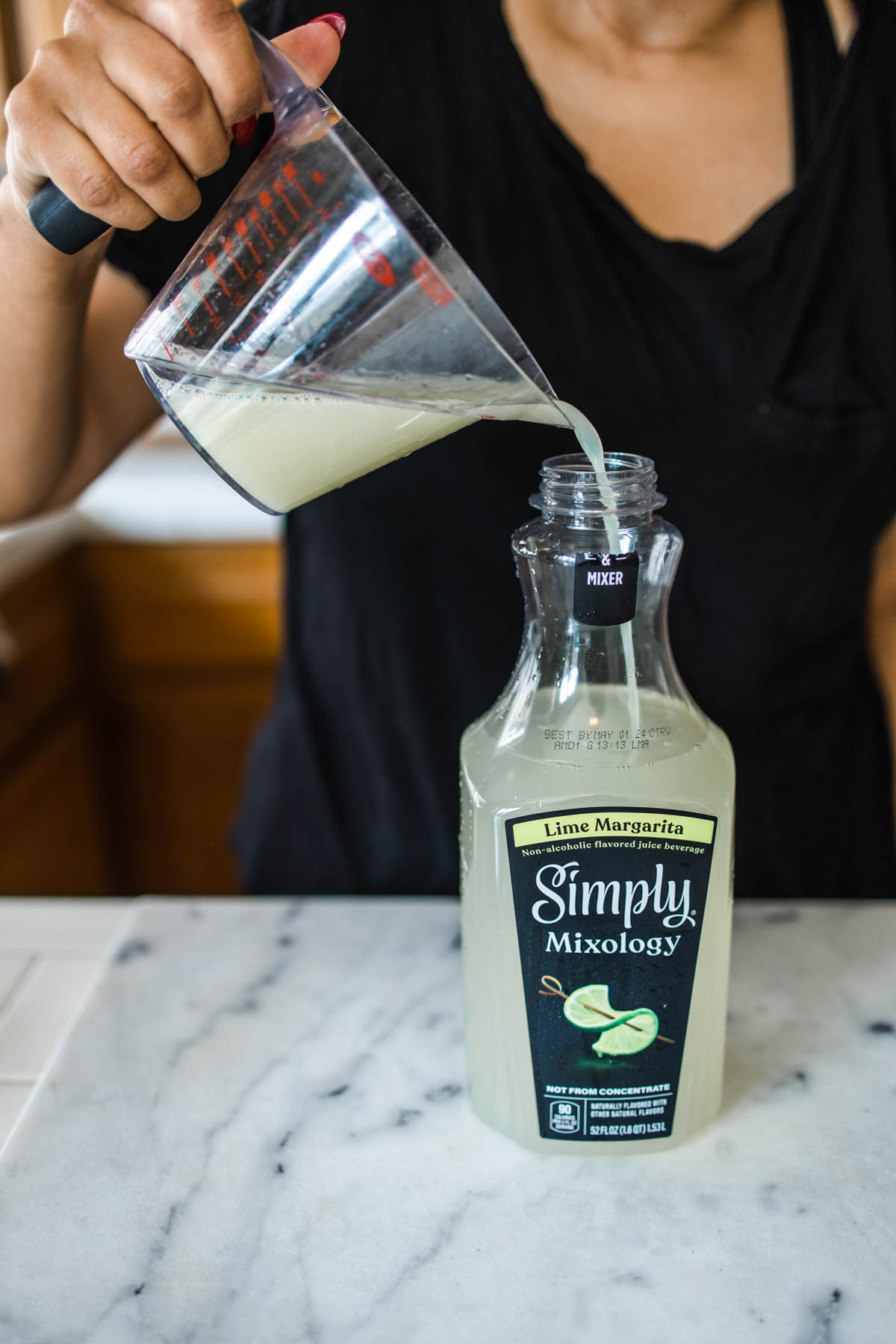 A woman pouring freshly squeezed lime juice into the bottle of Simply Margarita on top of a counter.