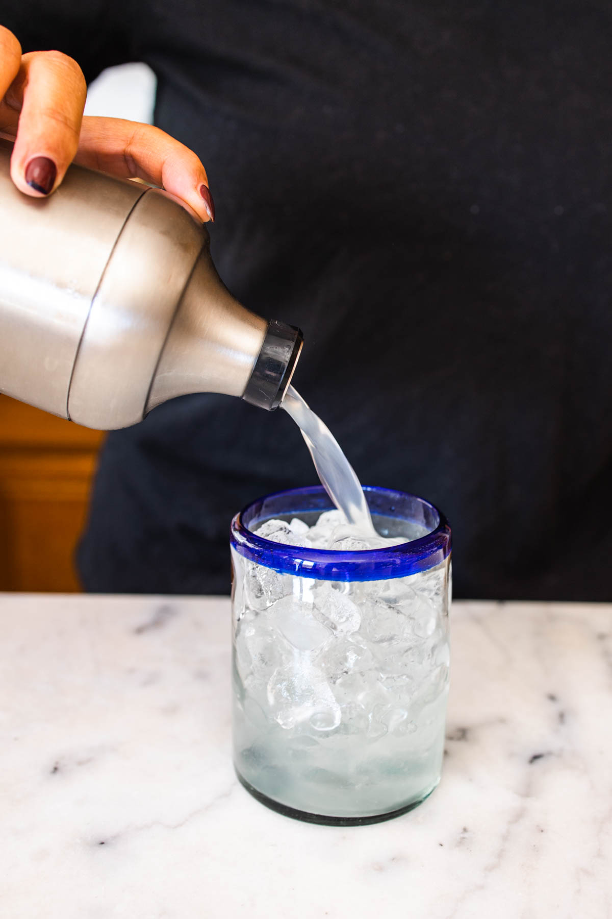 A person pouring the Seedlip margarita mixture into a blue-rimmed glass with ice.